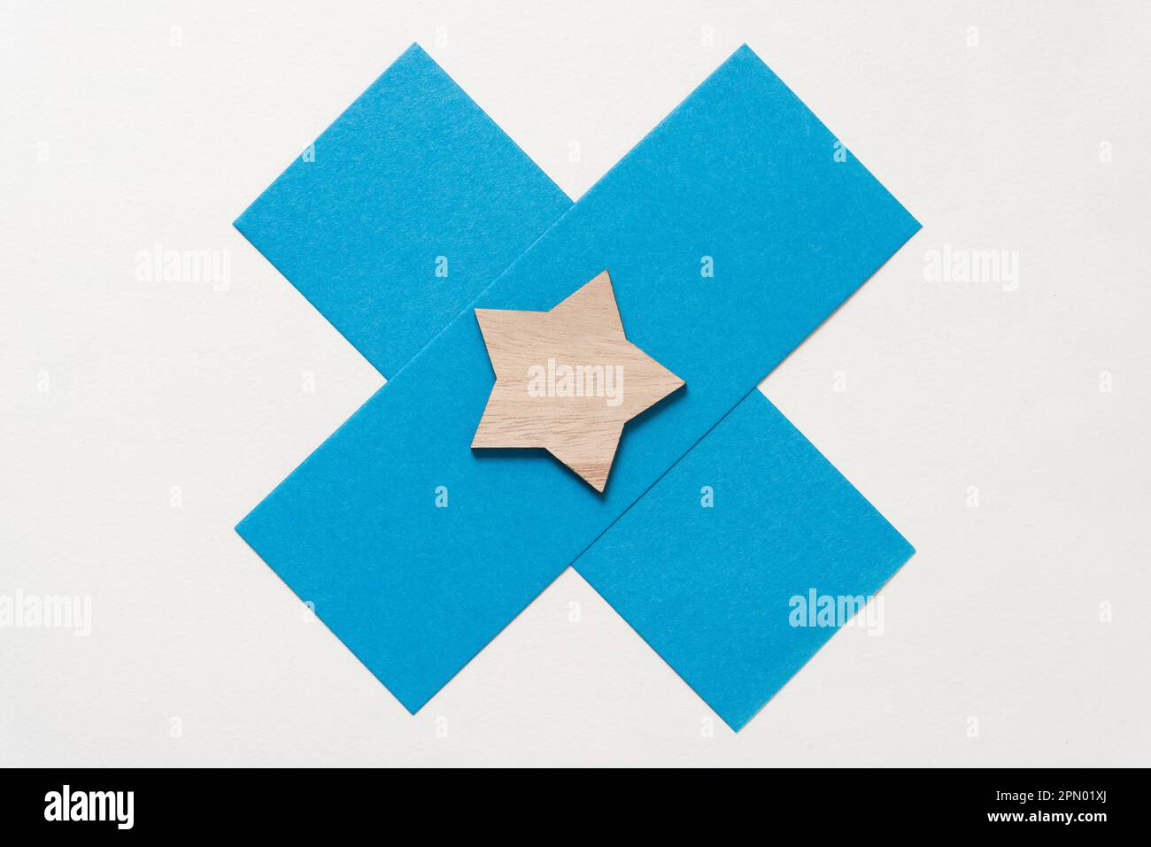 Forma a stella di legno semplice abbellimento su due fogli di carta blu disposti a forma di X o croce Foto Stock