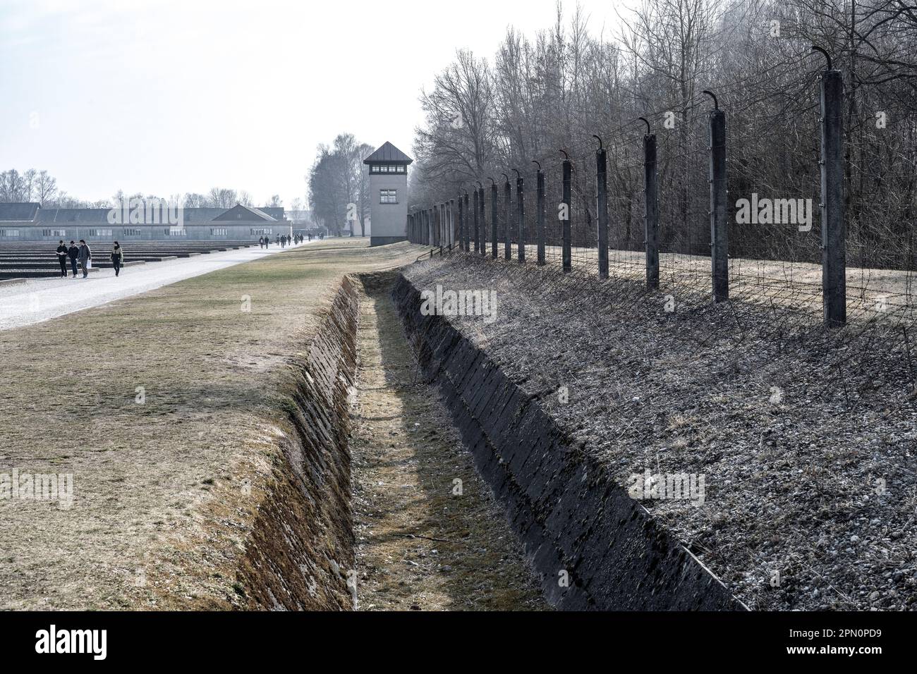 fossato e recinzione elettrica in filo spinato vicino ad una torre di guardia per impedire ai prigionieri di fuggire con le caserme in lontananza Foto Stock