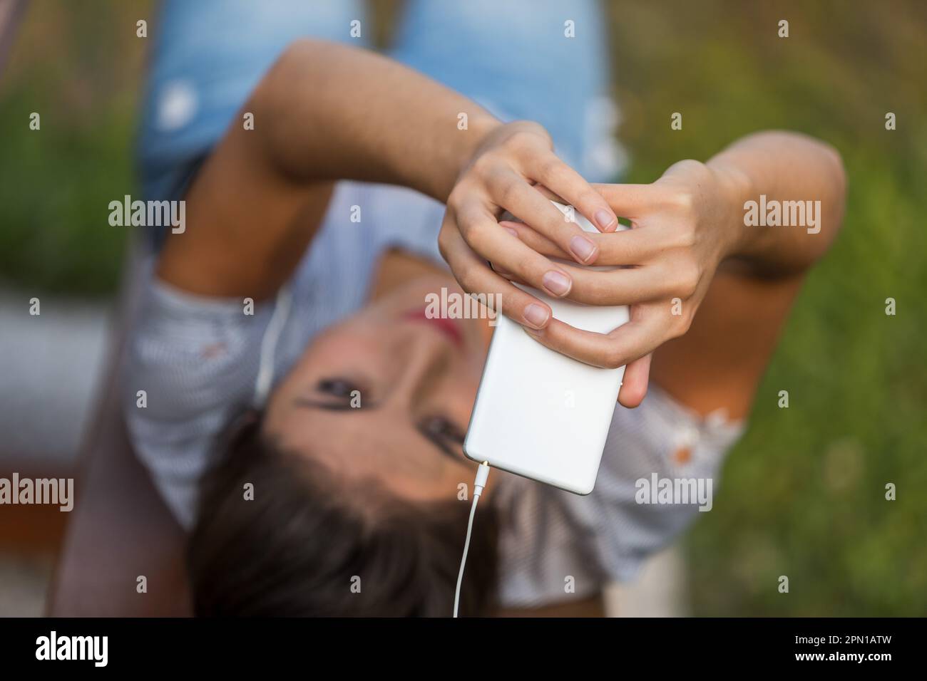 Una giovane donna con capelli castani scatta selfie o effettua una videochiamata utilizzando il suo smartphone bianco. Allunga le braccia per migliorare l'inquadratura durante l'uso Foto Stock