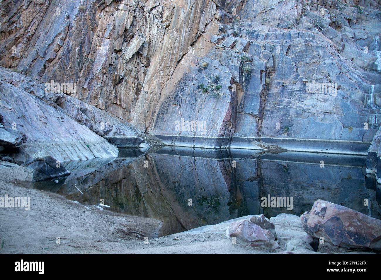 Riflessioni nella piscina sotto una cascata asciutta circondata da rocce con roccia in pendenza sulla sinistra. Foto Stock