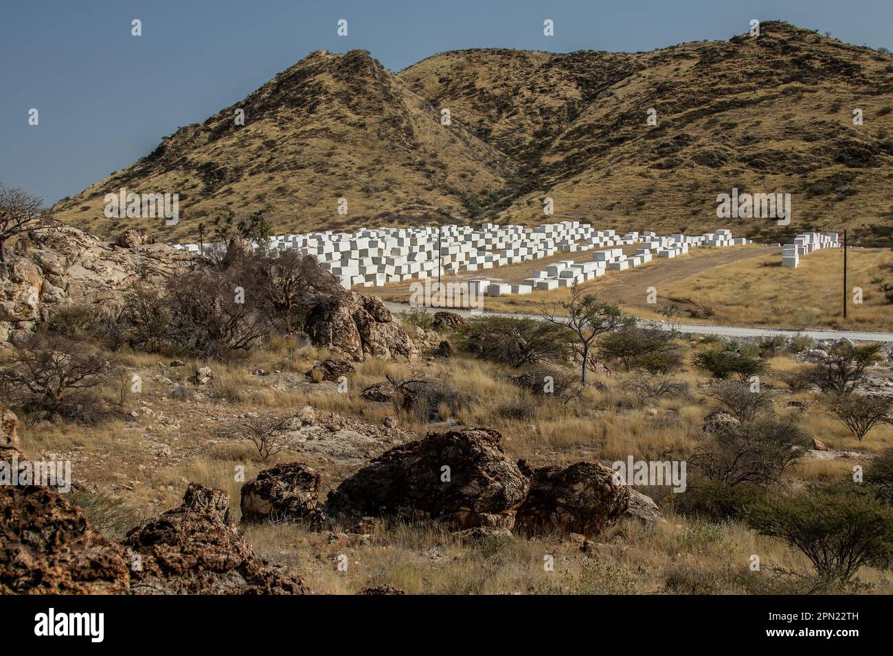 Blocchi di marmo bianco Namibiano, di rinoceronte impilati per la vendita su terreno pianeggiante di fronte ad una montagna in Namibia. Foto Stock