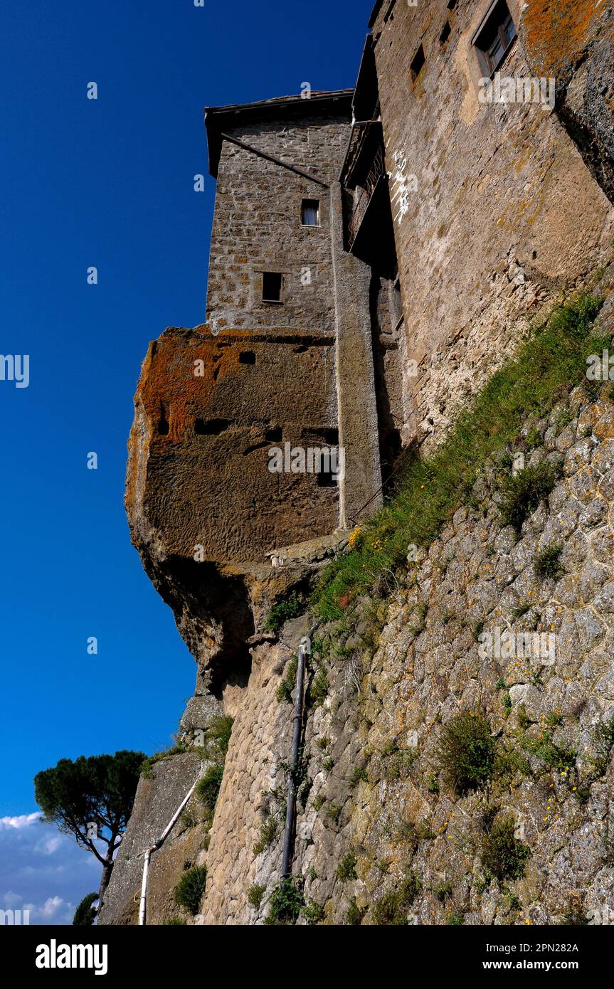 Un affioramento di roccia vulcanica sostiene tradizionali case in pietra che condividono una collina a Bomarzo, Lazio, Italia, con il Palazzo Orsini, un grande palazzo ducale rinascimentale costruito per la ricca famiglia Orsini nel 1500s. Il palazzo fu creato principalmente da Pier Francesco Orsini, comandante militare in pensione e patrono delle arti conosciuto nella sua vita come vicino Orsini. Foto Stock