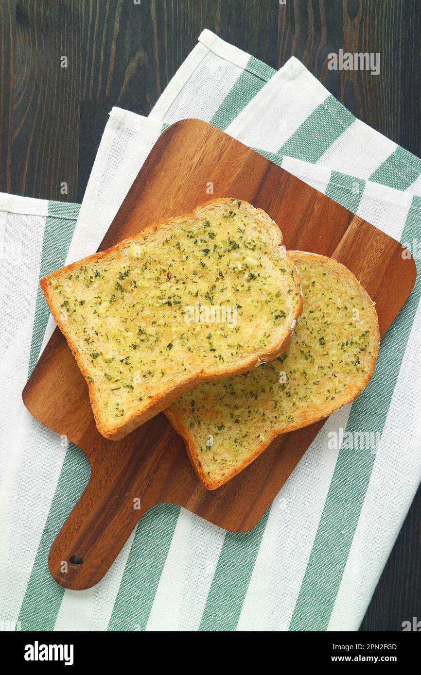 Coppia di toast al burro all'aglio su tavoletta di legno sul tavolo di legno nero Foto Stock