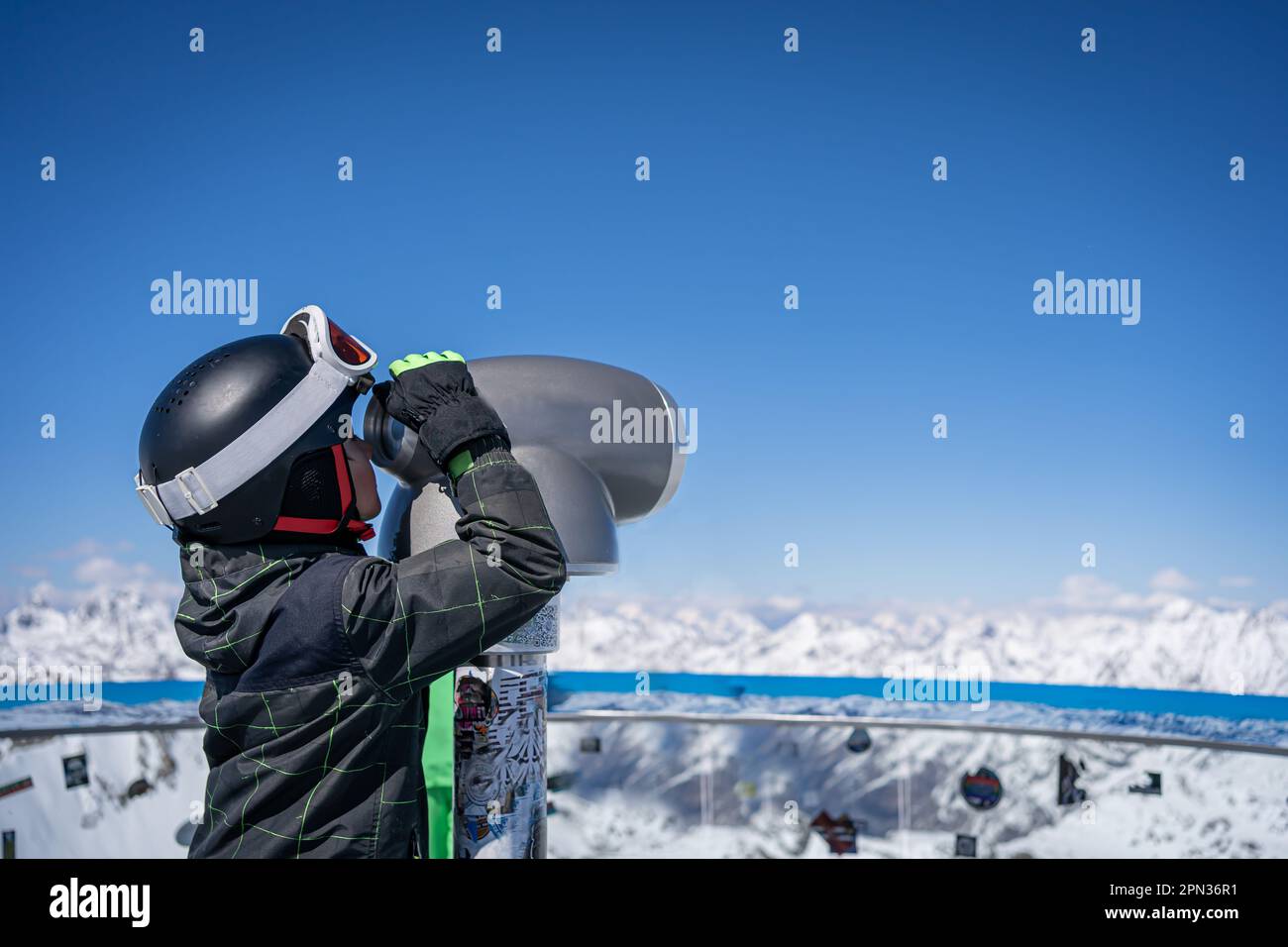 Un ragazzo in casco da sci guarda attraverso un telescopio sulle montagne in Austria, Tirolo Foto Stock