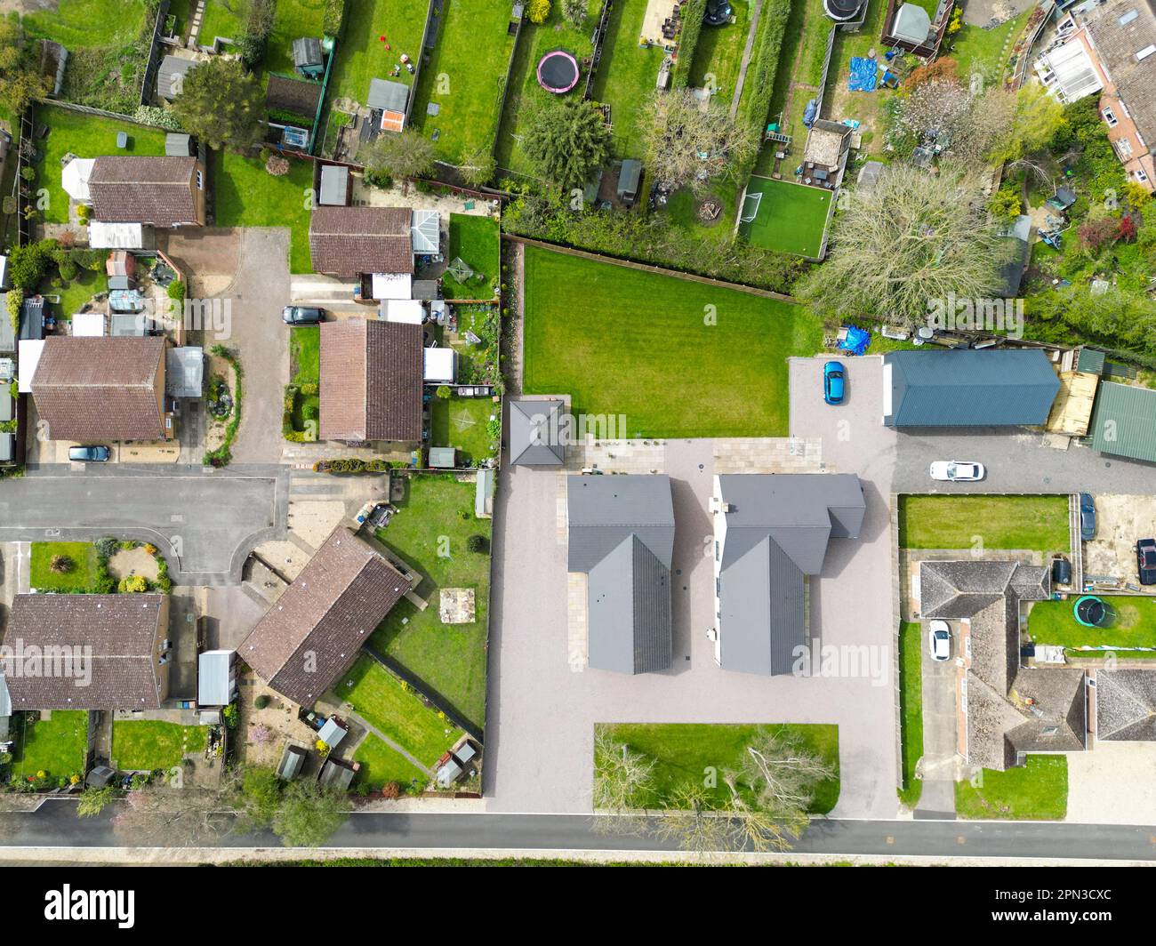 Vista aerea dall'alto verso il basso di una coppia di nuovi bungalow staccati visti adiacenti a case e giardini stabiliti. Foto Stock