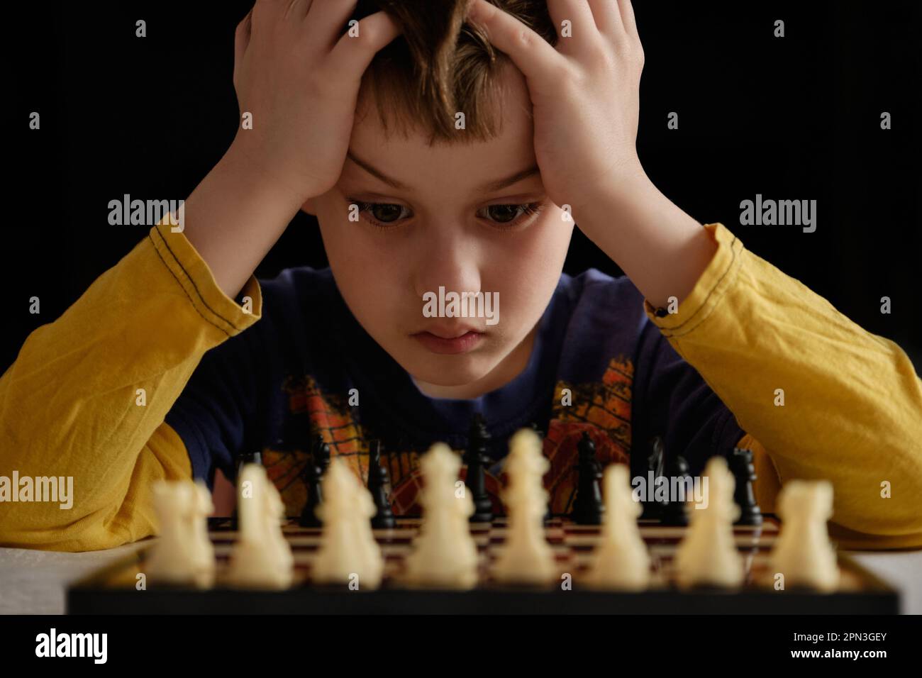 Carino bambino gioca a scacchi. Concetto di educazione, gioco intellettuale. Ragazzo concentrato che sviluppa la strategia degli scacchi. Torneo di scacchi, lezione, allenamento. Foto Stock