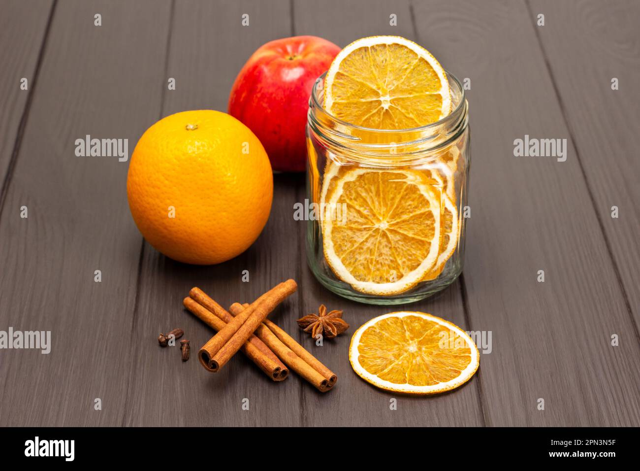 Scaglie di arancia in un vaso di vetro. Arancia cruda e mela fresca. Bastoncini di cannella e anice stellato sul tavolo. Spazio di copia. Sfondo di legno scuro. Foto Stock