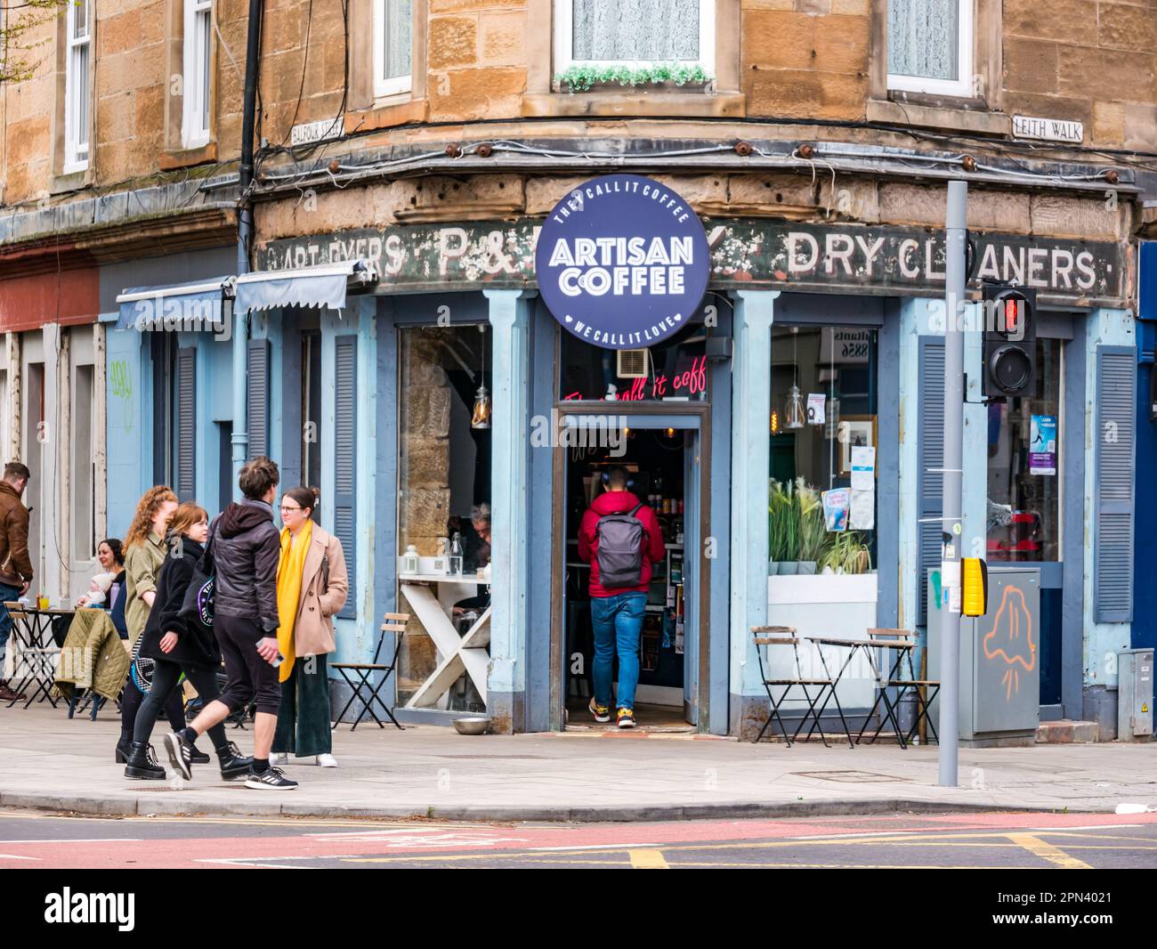 Persone ai tavoli da marciapiede in una caffetteria artigianale con il cartello fantasma Dry Cleaners, leith Walk, Edinburgo, Scozia, Regno Unito Foto Stock