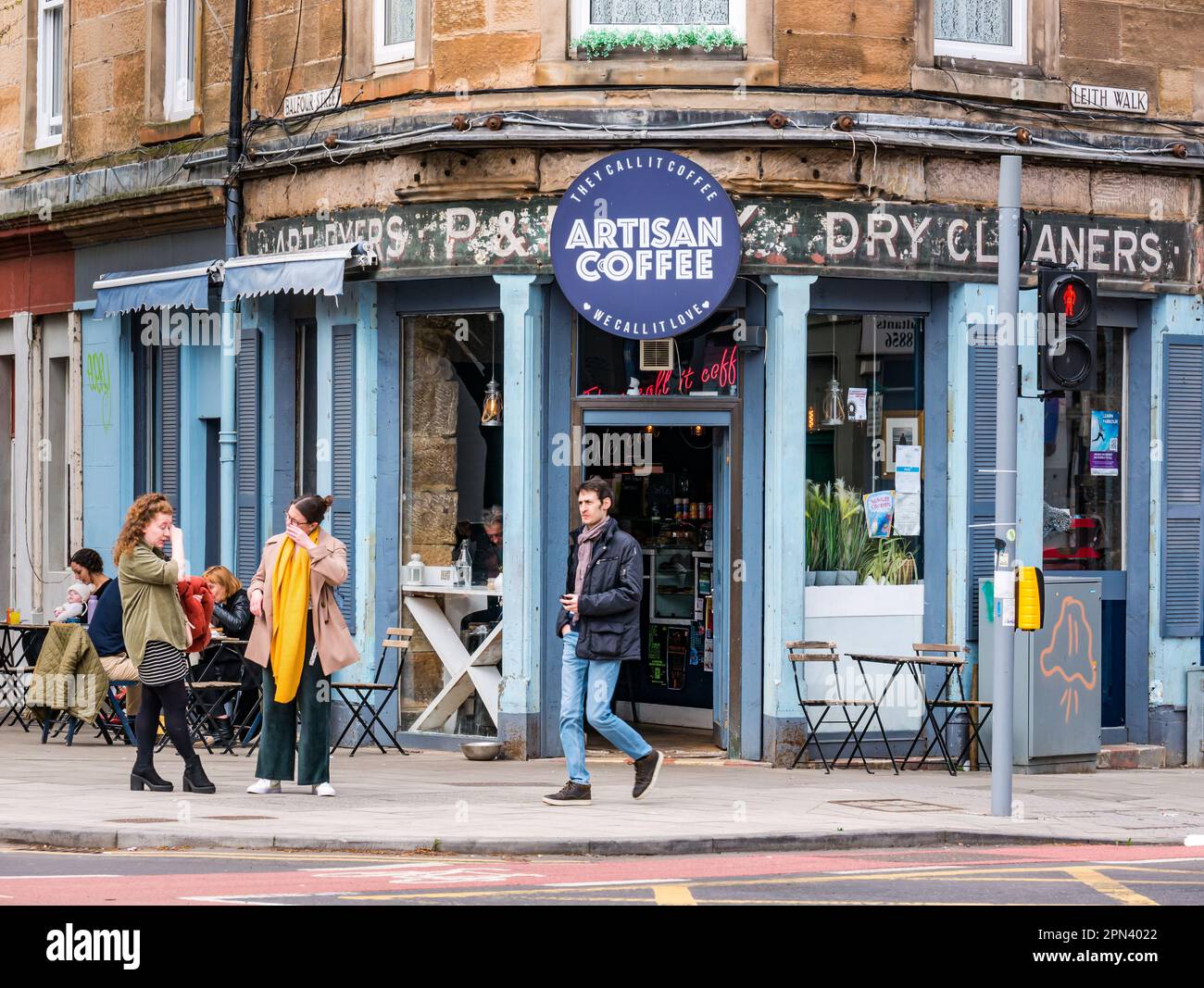 Persone ai tavoli da marciapiede in una caffetteria artigianale con il cartello fantasma Dry Cleaners, leith Walk, Edinburgo, Scozia, Regno Unito Foto Stock