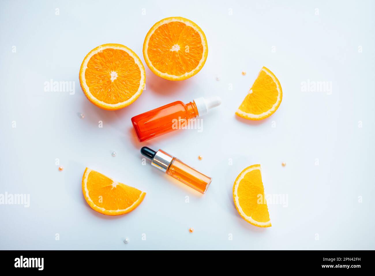 Concetto cosmetico di cura della pelle della vitamina C - siero organico in una bottiglia e fette arancioni su fondo bianco. Foto Stock