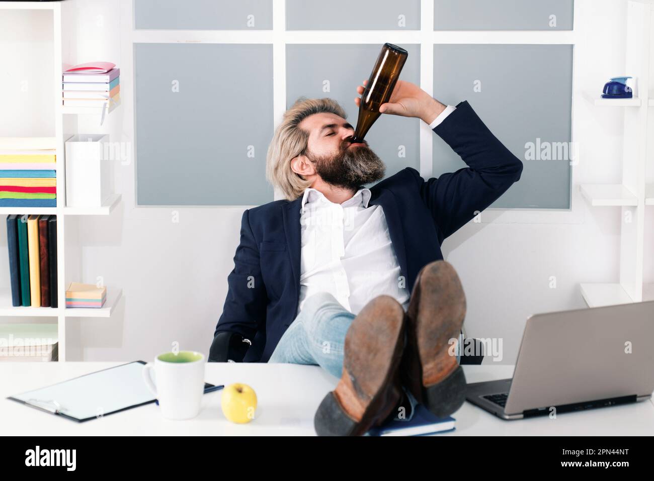 Impiegato che beve birra in ufficio. Divertente lavoro di ufficio che va pazzo di alcol. Ubriaco dipendente business manager alzarsi seduta in sedia. Foto Stock