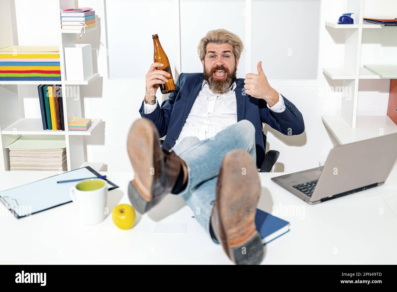Ubriaco lavoratore in ufficio. Dipendente ubriaco bearded divertente in ufficio. Buon lavoratore con una bottiglia di birra. Foto Stock