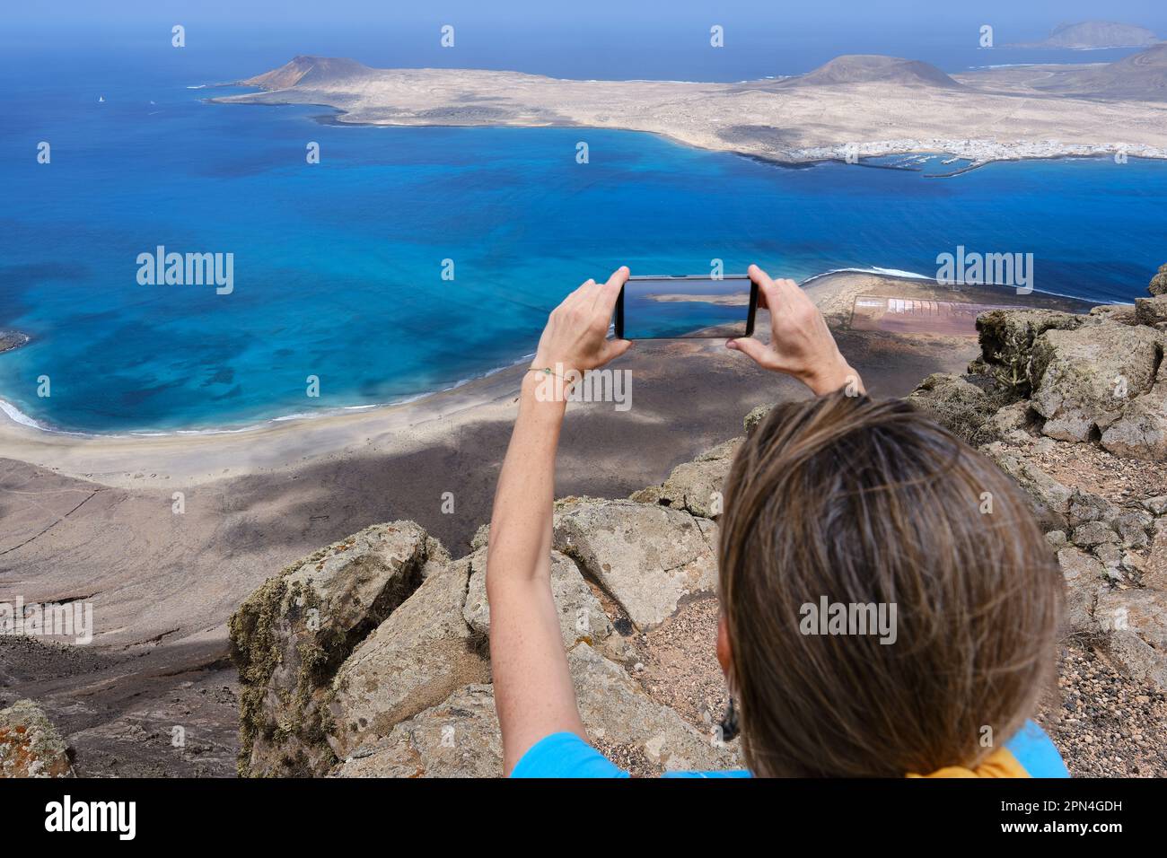 Una donna escursionista fotografando con il suo smartphone dalla cima di una collina la Graciosa Island. Isole Canarie Foto Stock