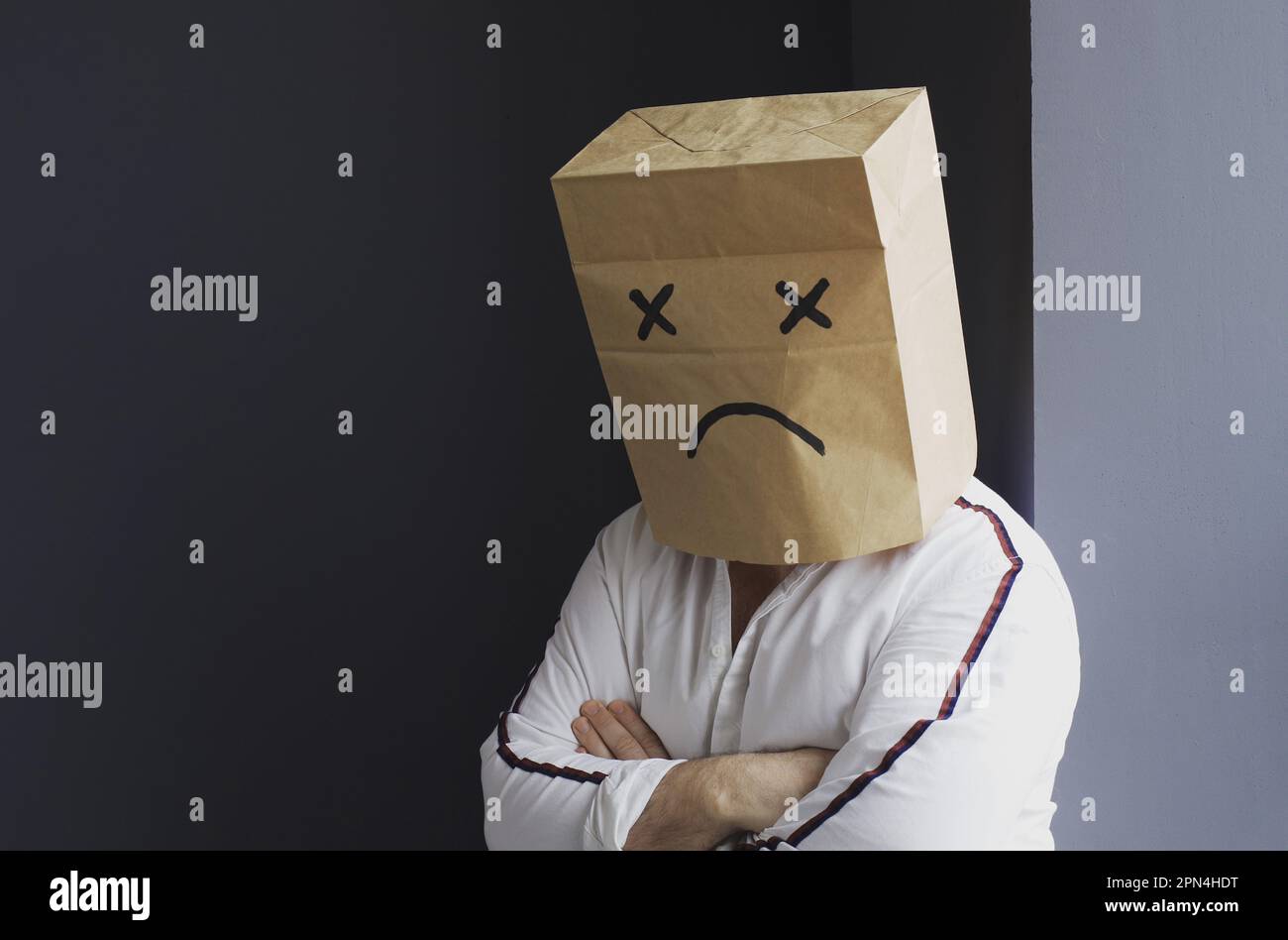 Un uomo triste in una camicia bianca con una borsa sulla testa, con un volto triste e sorridente disegnato, si trova contro il muro e grida. Foto Stock