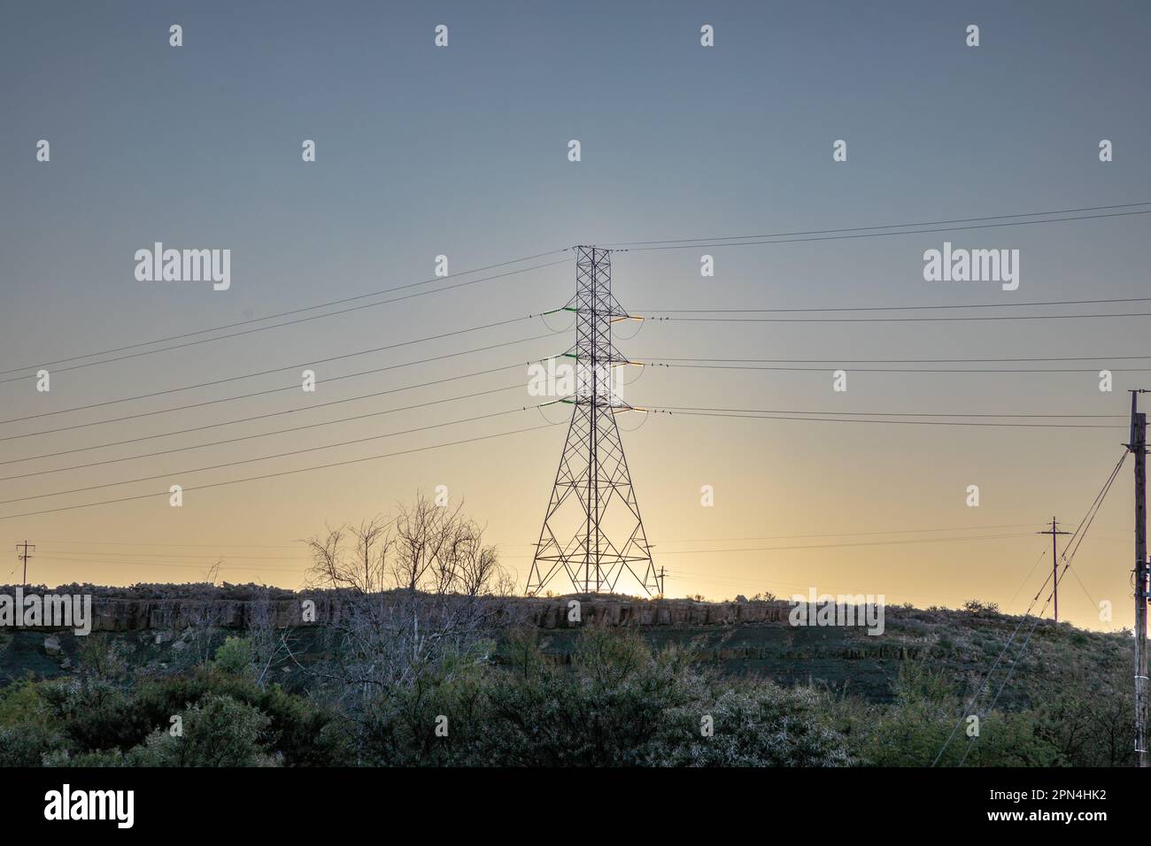 Linee elettriche ad alta tensione su una collina al tramonto con il sole che tramonta dietro il pilone, torre di trasmissione elettrica ad alta tensione nella regione di Karoo di così Foto Stock