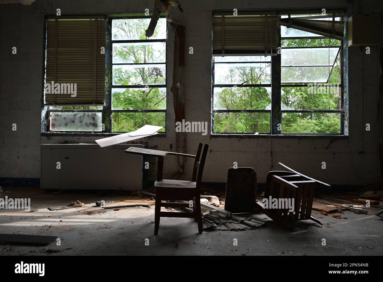 Un paio di banchi di studenti scartati sono rimasti in un'aula piena di detriti in una scuola abbandonata dal 2001. Foto Stock