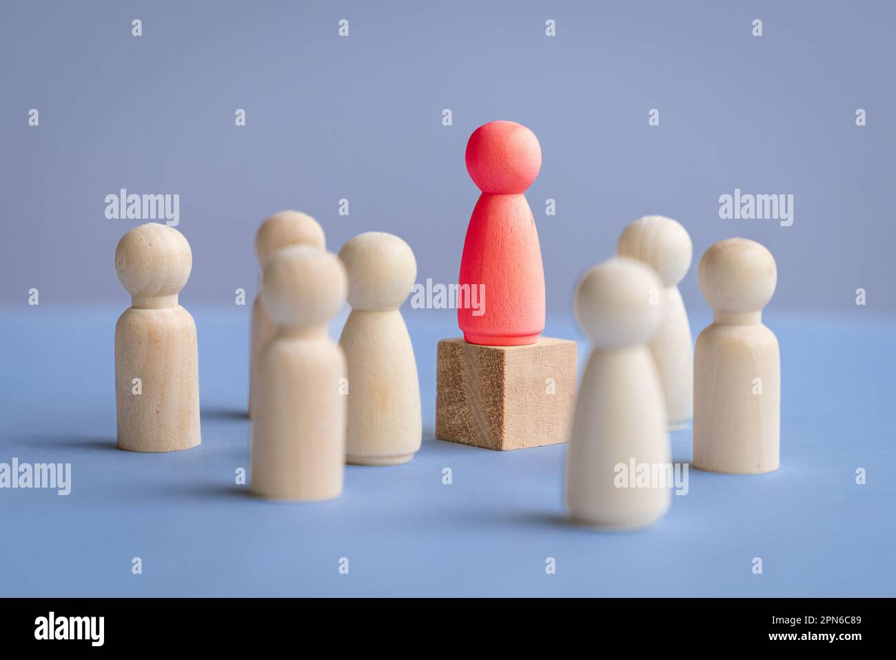 Bambola rossa di legno in piedi su un podio quadrato circondato da altre bambole. Concetto di leadership femminile. Foto Stock