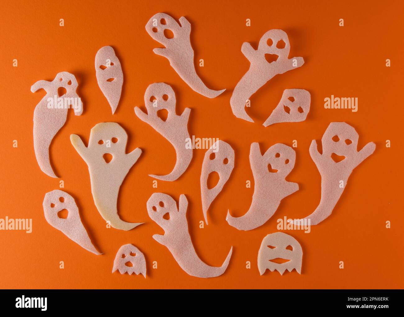 Fantasmi bianchi bambini di mestiere per Halloween. Immagine fantasma della carta di avvolgimento su sfondo arancione vista dall'alto. Un mostro pauroso e divertente giocattolo con le tue mani. Fumetto Creepy Whisper. Fai-da-te fatto a mano. Impostare i caratteri boo Foto Stock