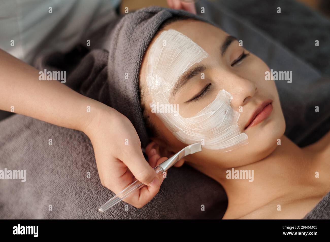 Estetista applicare maschera di argilla bianca sul viso della giovane donna Foto Stock