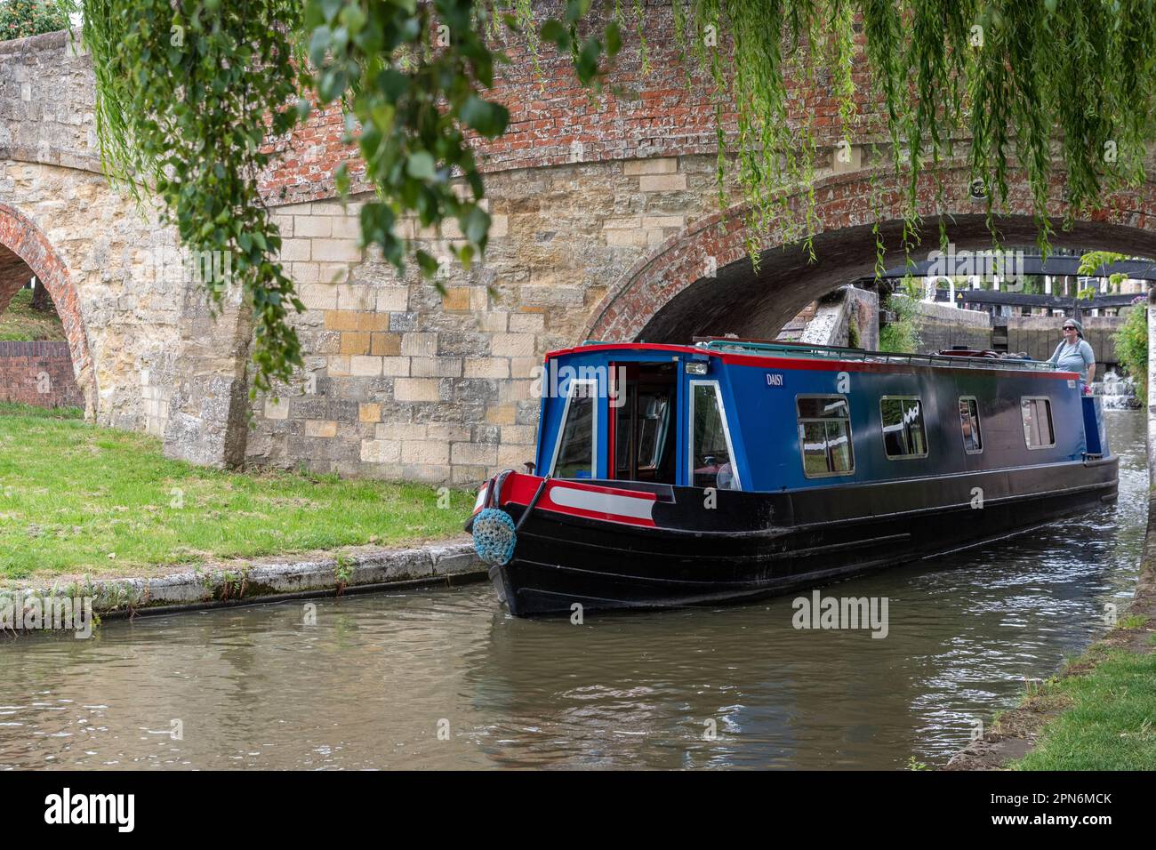 Narrowboat che naviga sotto un ponte sul canale a Stoke Bruerne, Northamptonshire, Regno Unito Foto Stock