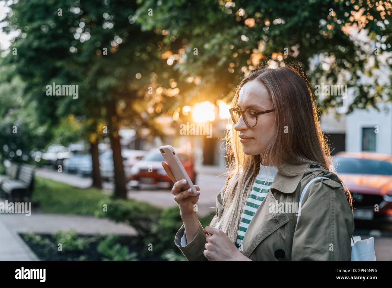 Donna con gli occhiali usa lo smartphone la sera in città Foto Stock