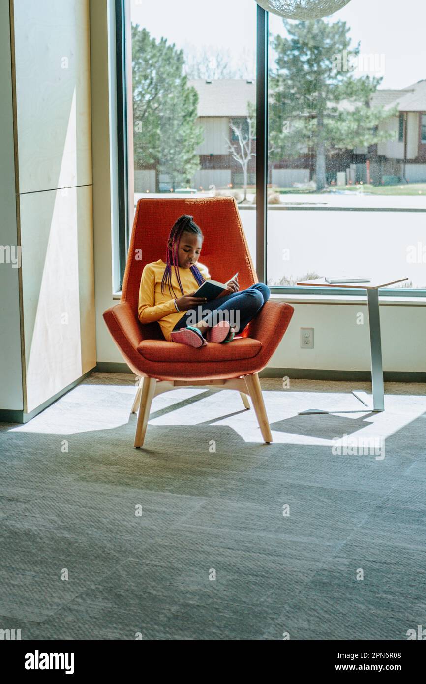 Giovane ragazza che legge un libro in un angolo soleggiato Foto Stock