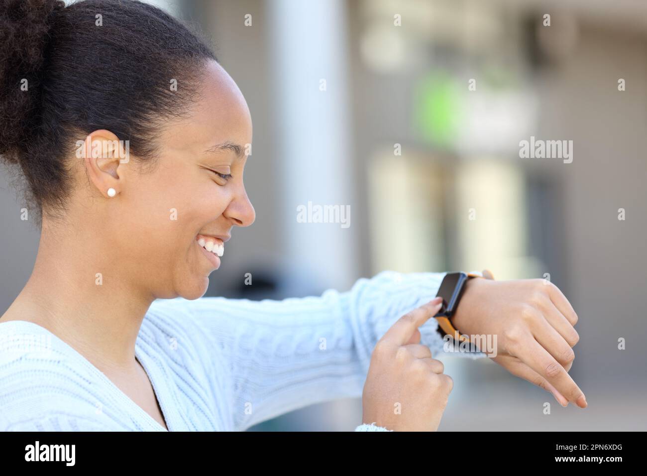 Profilo di una donna nera felice che controlla smartwatch in strada Foto Stock