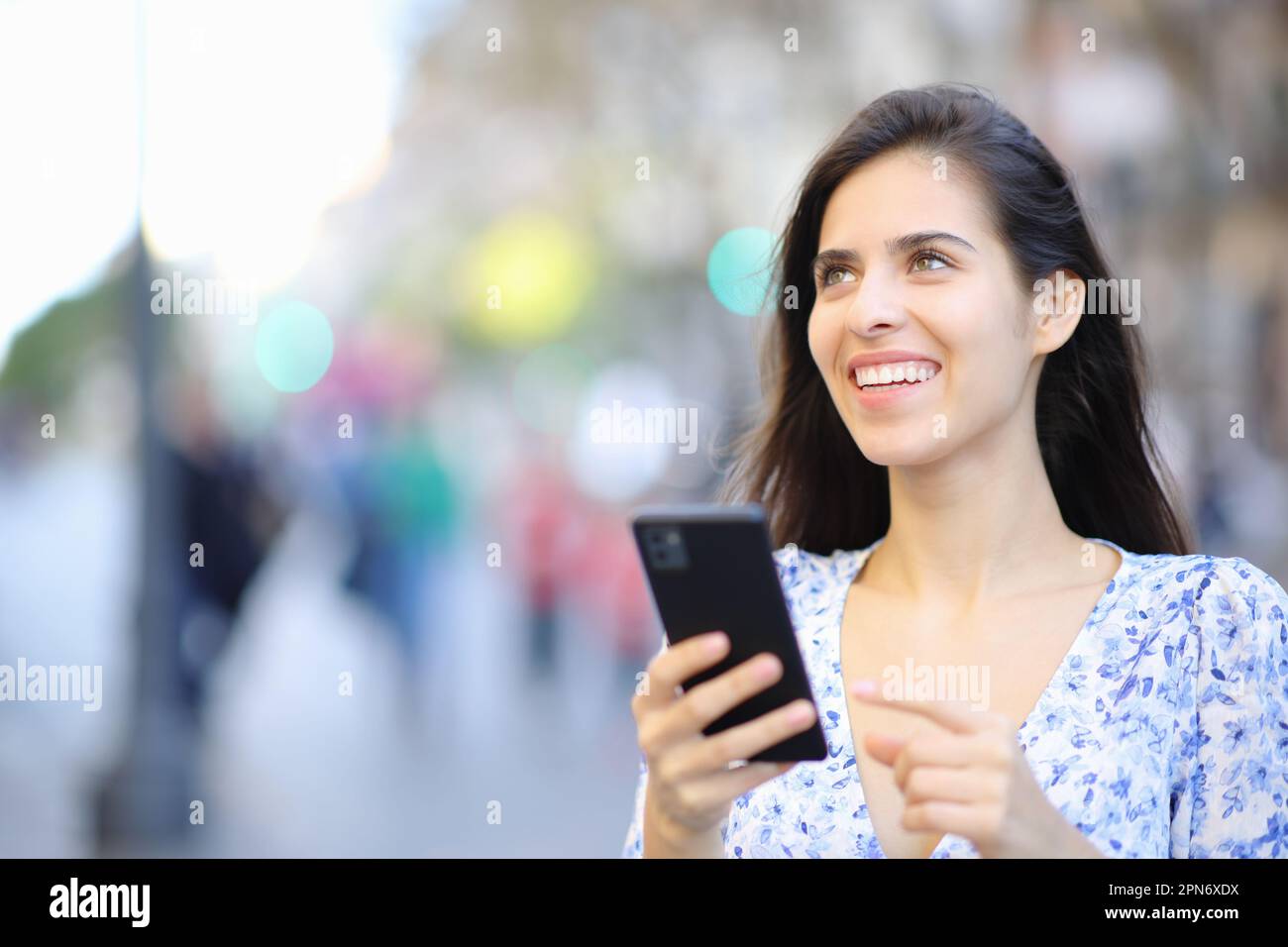 Donna felice che tiene il telefono delle cellule guarda in su nella strada Foto Stock