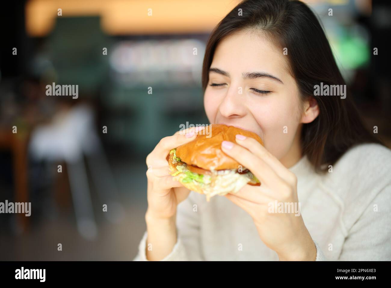 Donna felice che mangia hamburger in un ristorante Foto Stock