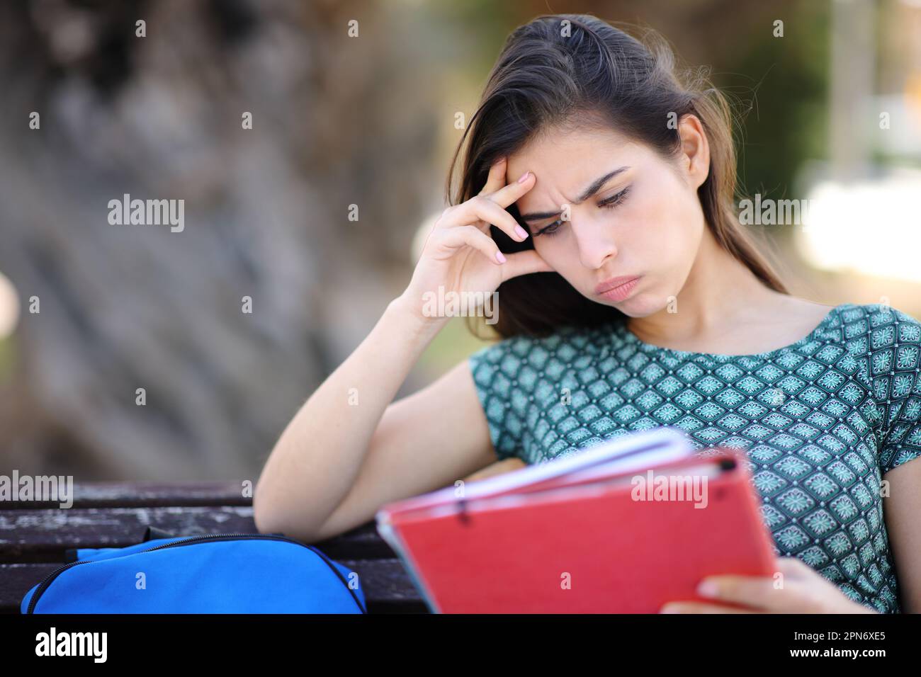 Studente frustrato cercando di imparare sititng su una panchina in un parco Foto Stock