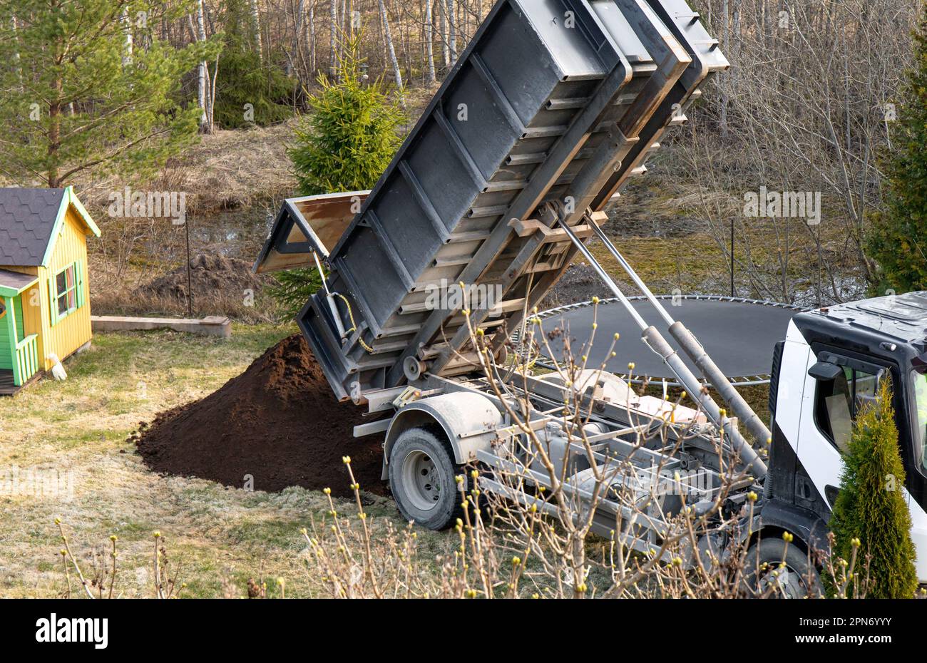 Camion di consegna che versa terra di giardino nero di grado superiore dalla scatola al giardino domestico in primavera. Foto Stock