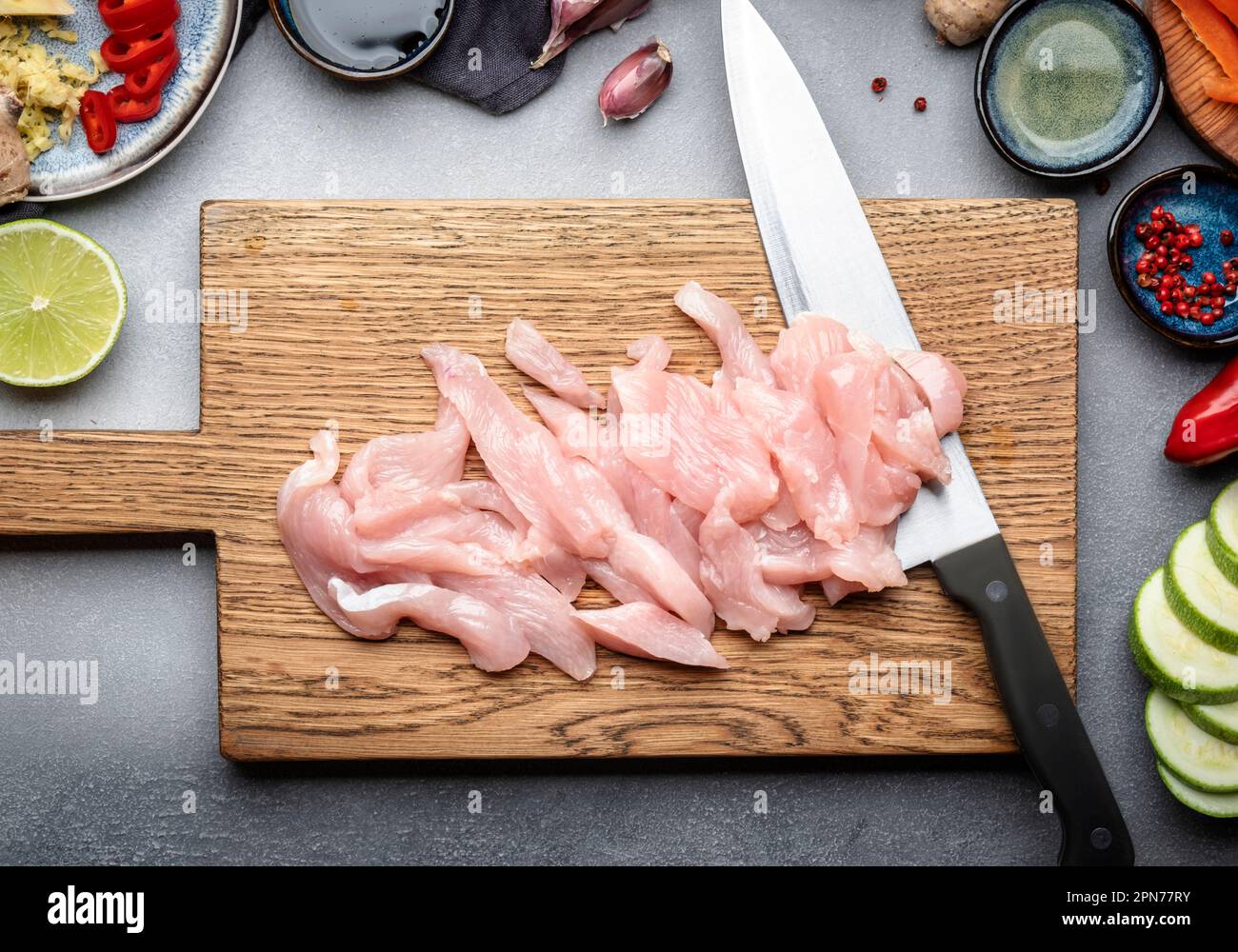 Cibo sfondo. Filetto di pollo a fette e coltello dello chef sul tagliere., verdure, zenzero, lime, peperoncino, aglio, salsa di soia e aceto di riso Foto Stock