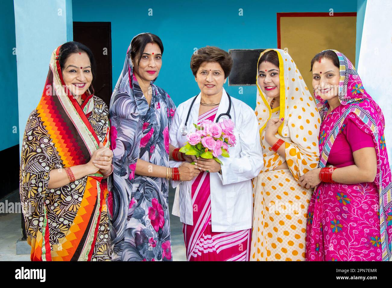 Gruppo di donne indiane tradizionali che indossano sari ringraziando e salutando medico dando bouquet di fiori, concetto di empowerment donna Foto Stock
