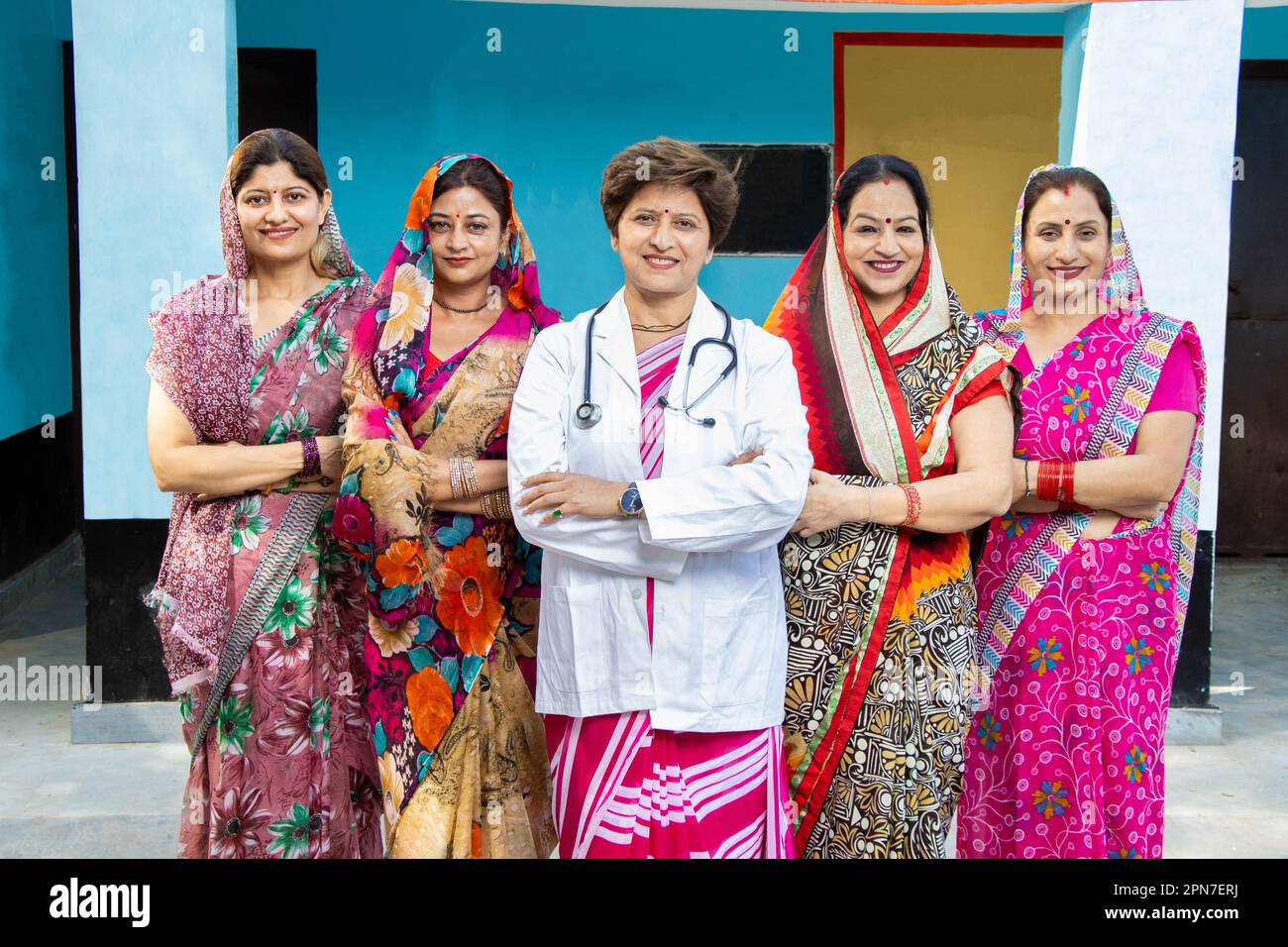 Medico fiducioso Lady in piedi con un gruppo di tradizionali donne indiane rurali che indossano sri con la loro croce di braccia. Concetto di empowerment della donna. Foto Stock