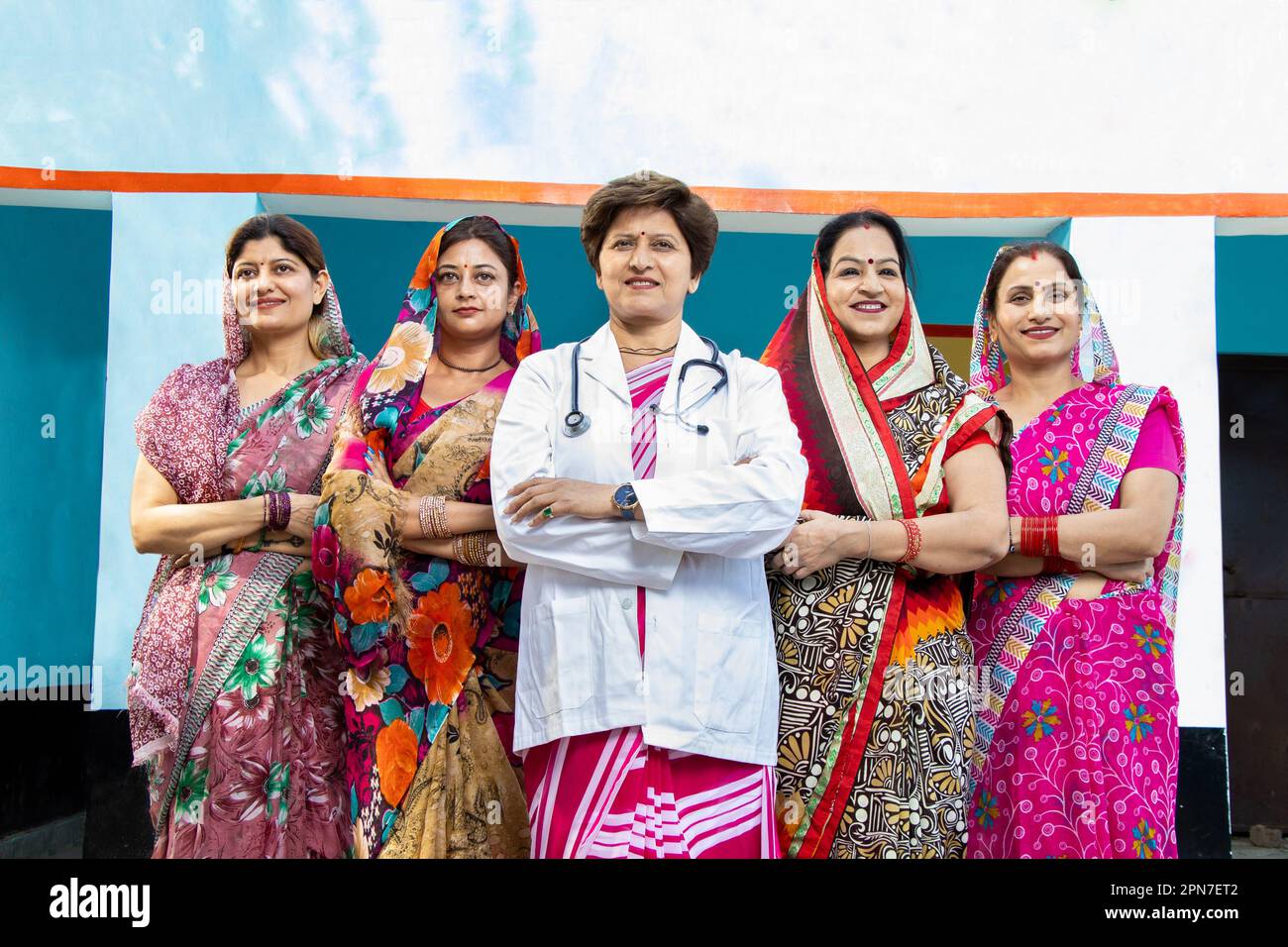 Medico fiducioso Lady in piedi con un gruppo di tradizionali donne indiane rurali che indossano sri con la loro croce di braccia. Concetto di empowerment della donna. Angolo basso Foto Stock
