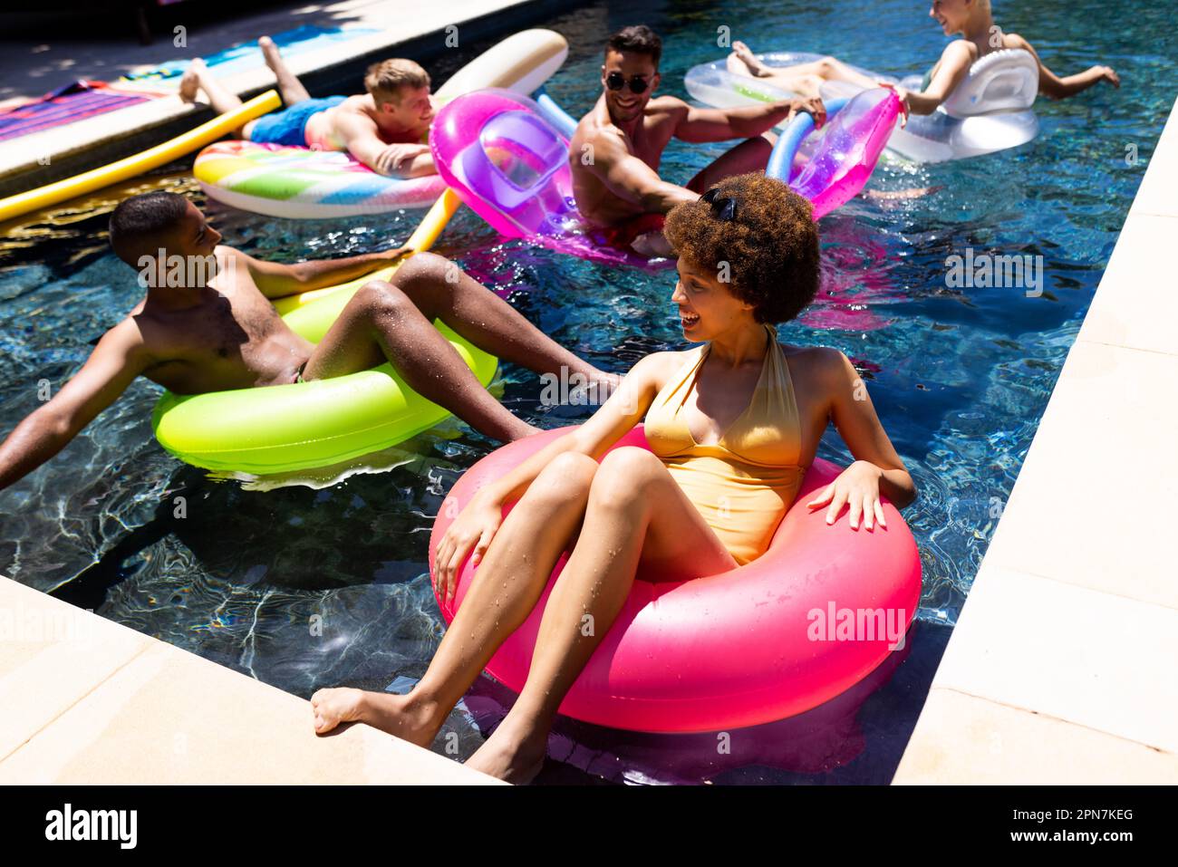 Felice gruppo di amici diversi che hanno partito in piscina, utilizzando anelli da nuoto in piscina in giardino Foto Stock Felice gruppo di amici diversi che hanno partito in piscina, utilizzando anelli da nuoto in piscina in giardino Foto Stock