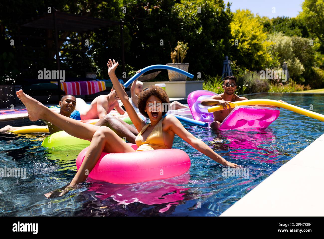 Felice gruppo di amici diversi che hanno partito in piscina, utilizzando anelli da nuoto in piscina in giardino Foto Stock Felice gruppo di amici diversi che hanno partito in piscina, utilizzando anelli da nuoto in piscina in giardino Foto Stock