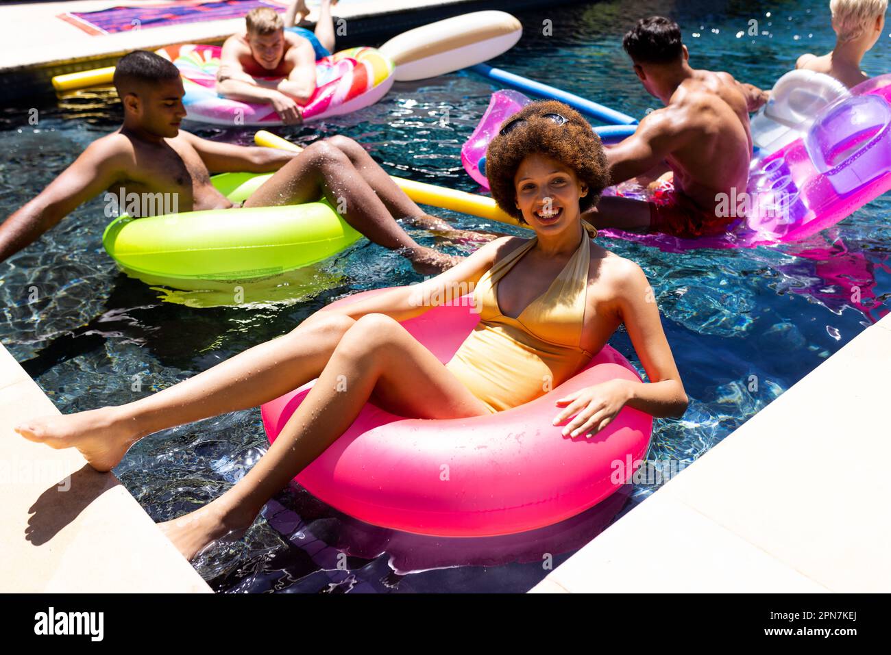 Felice gruppo di amici diversi che hanno partito in piscina, utilizzando anelli da nuoto in piscina in giardino Foto Stock Felice gruppo di amici diversi che hanno partito in piscina, utilizzando anelli da nuoto in piscina in giardino Foto Stock