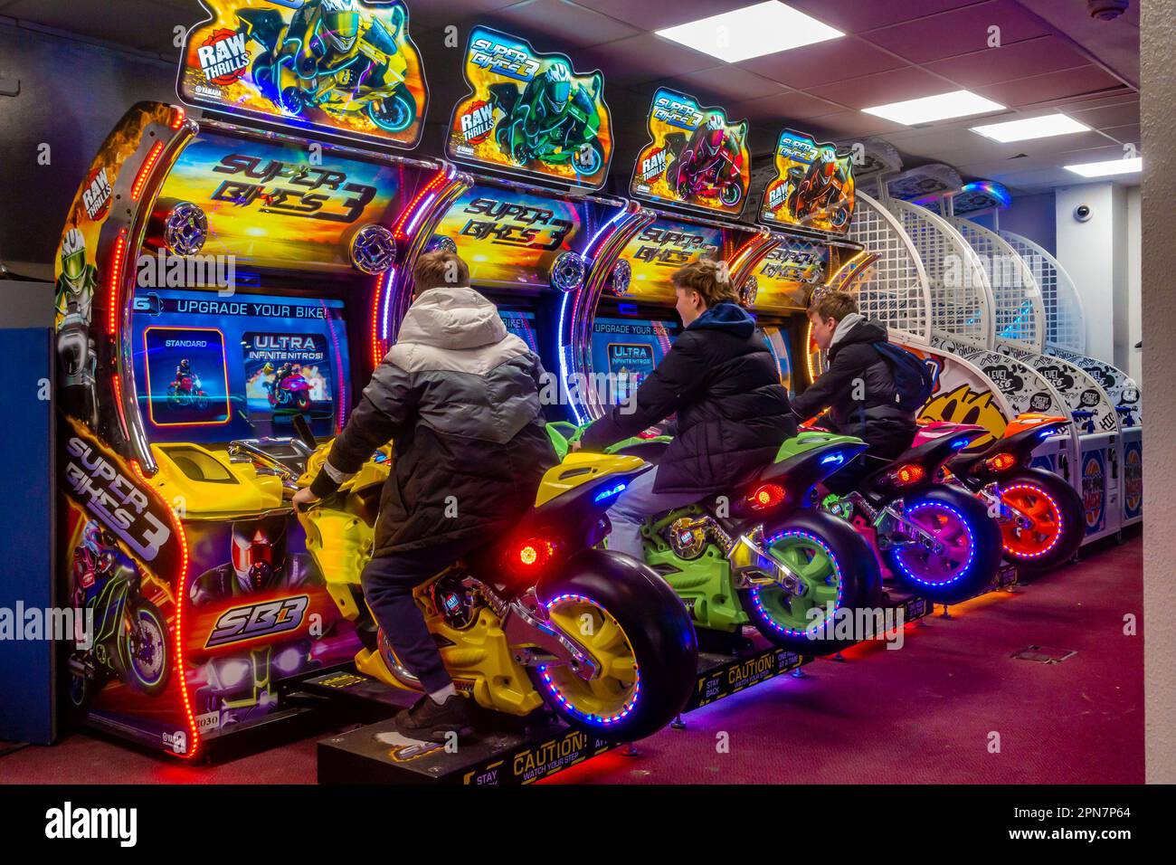 Amici adolescenti che giocano insieme su un gioco arcade di corse di moto in una galleria di divertimenti a Bournemouth, Regno Unito Foto Stock