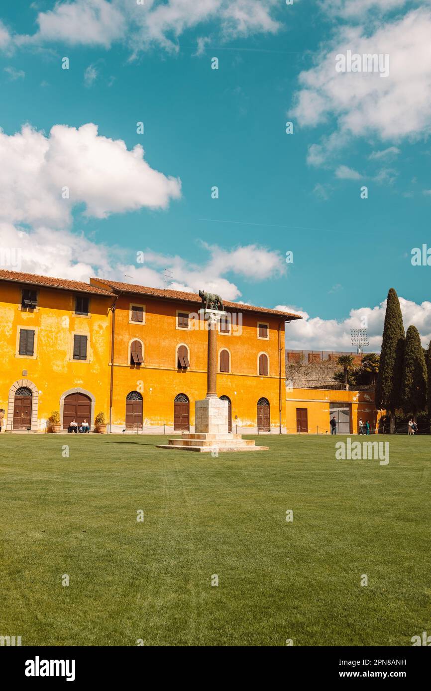 Pisa, Italia - 18 marzo 2023: Palazzo dell'Opera, statua di Angelo Caduto, monumento di Lupa capitolina in piazza con prato verde, cielo blu Foto Stock