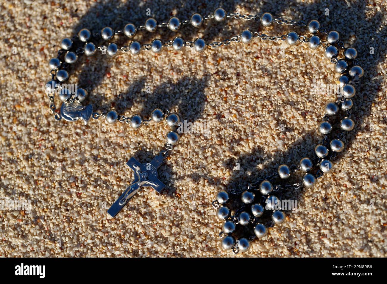 Un crocifisso d'argento e un rosario con perle parzialmente sepolte nella sabbia. Concetto di religione, fede e spiritualità. Foto Stock