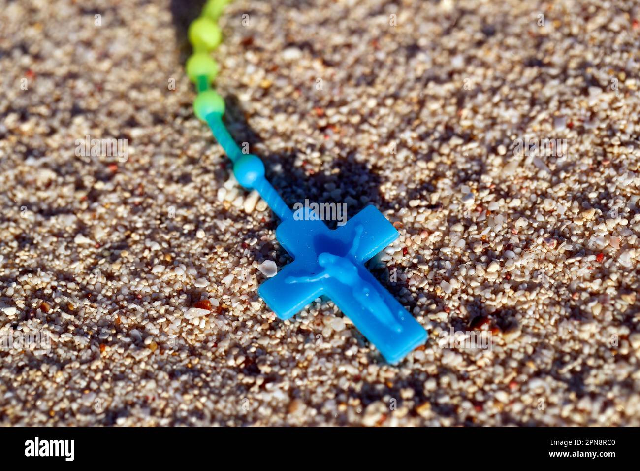 Un crocifisso di plastica e un rosario con perle parzialmente sepolte nella sabbia. Concetto di religione, fede e spiritualità. Foto Stock