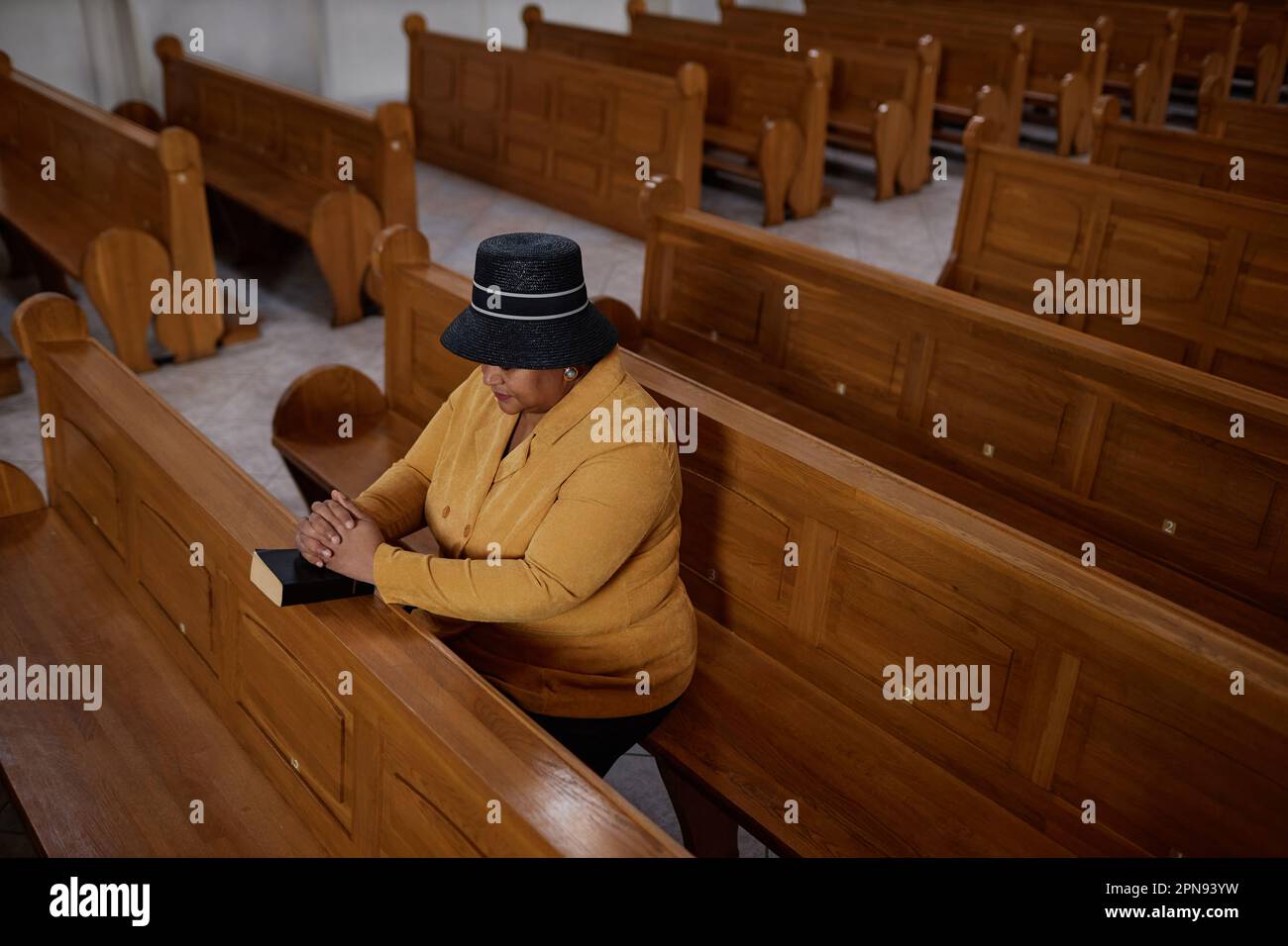 Vista ad alto angolo di un'elegante donna matura seduta su una panchina con la Bibbia e pregando durante il ministero in chiesa Foto Stock