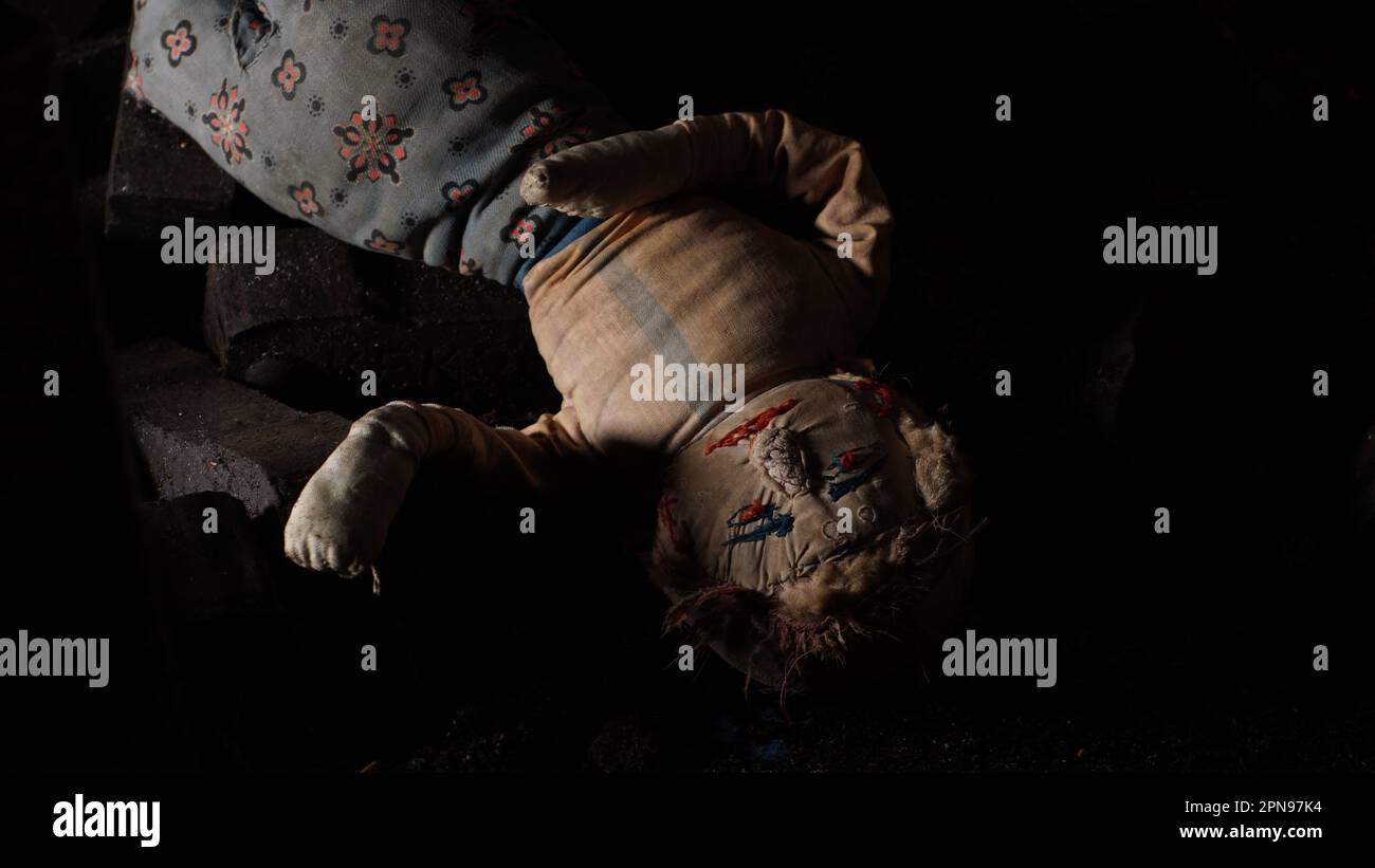 Una vecchia bambola di strana stesa con la testa giù nella cantina su un mucchio di bricchettini di lignate. Fa un'impressione trascurata e creepy. Foto Stock