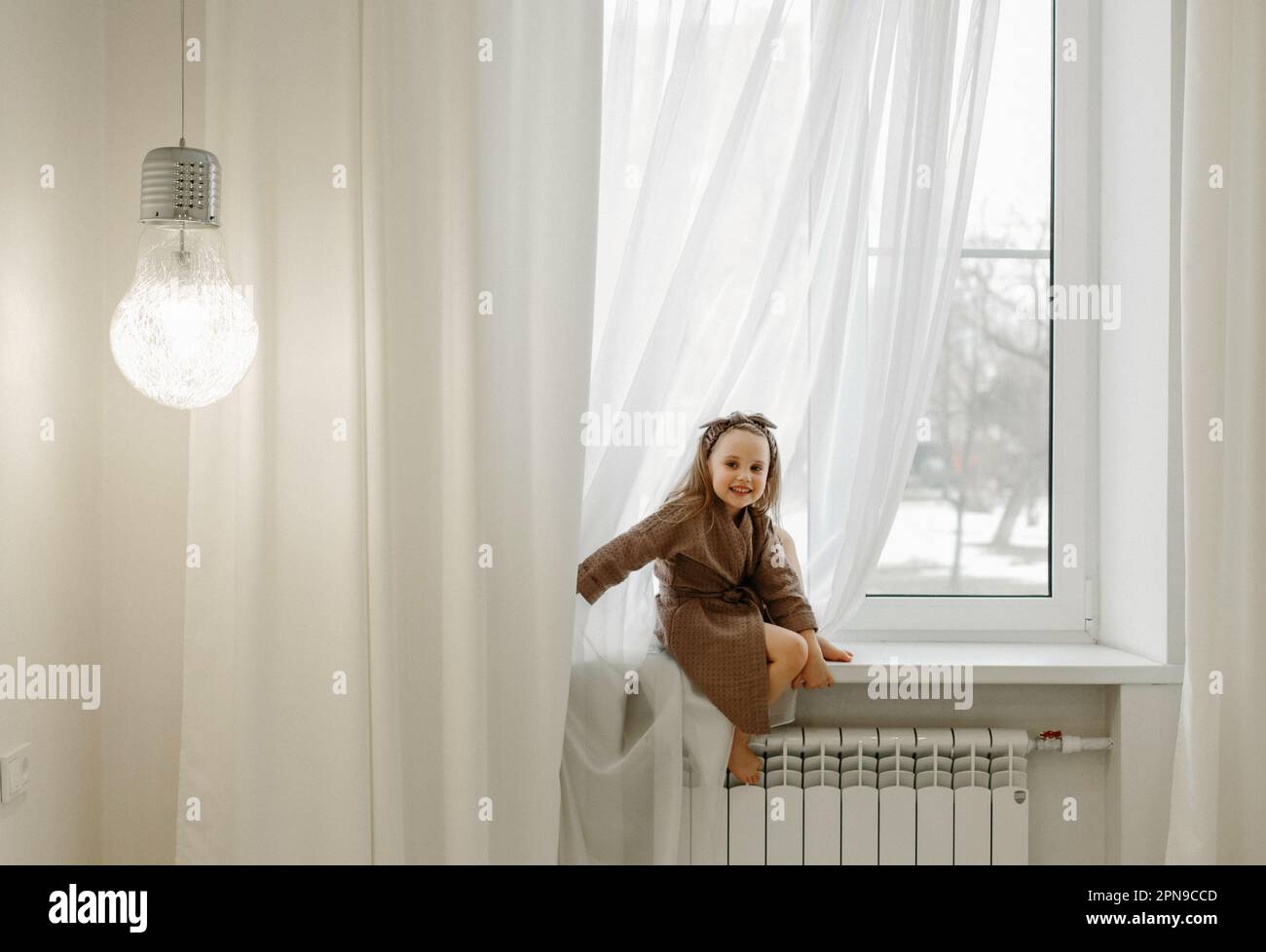 Ritratto di una bambina in vestaglia marrone, seduta sul davanzale. Foto Stock