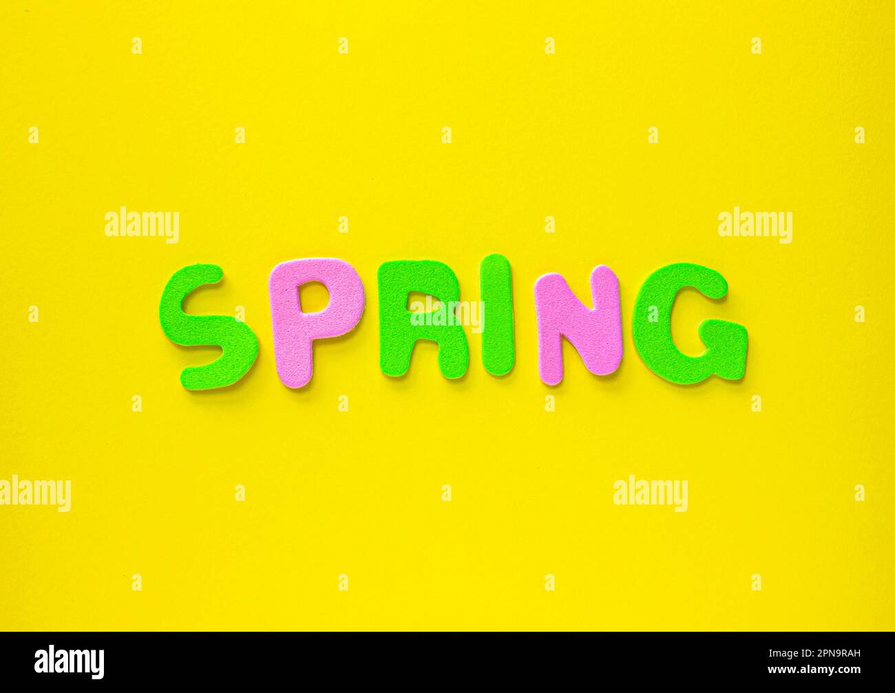 Le lettere colorate che scortano fuori primavera su sfondo giallo con spazio di copia. Biglietto d'auguri con lettere colorate Primavera su sfondo giallo. Foto Stock