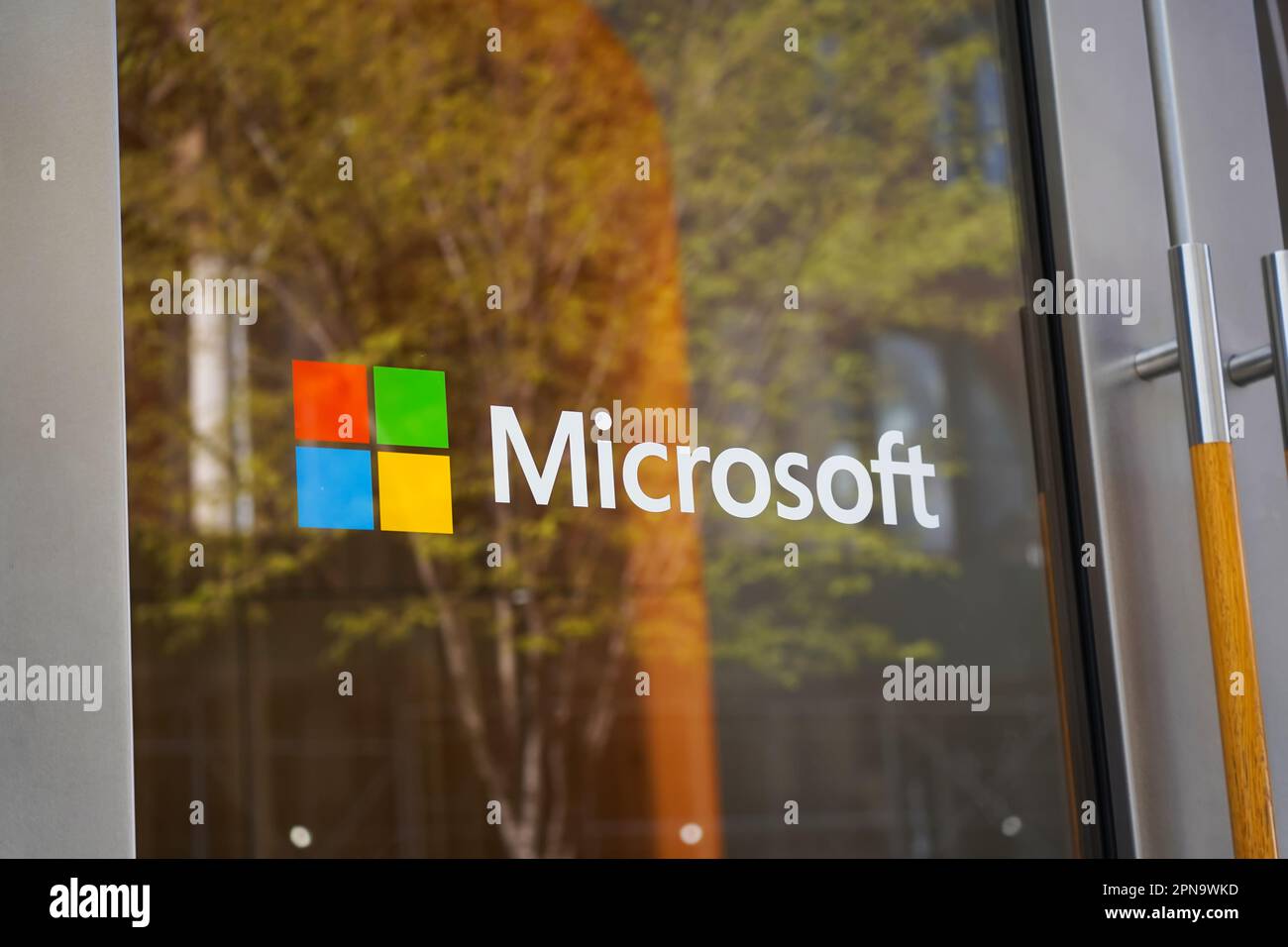 New York, NY - 9 aprile 2023: Logo Microsoft sulla porta di vetro del negozio SoHo Manhattan con riflesso verde dell'albero. Foto Stock