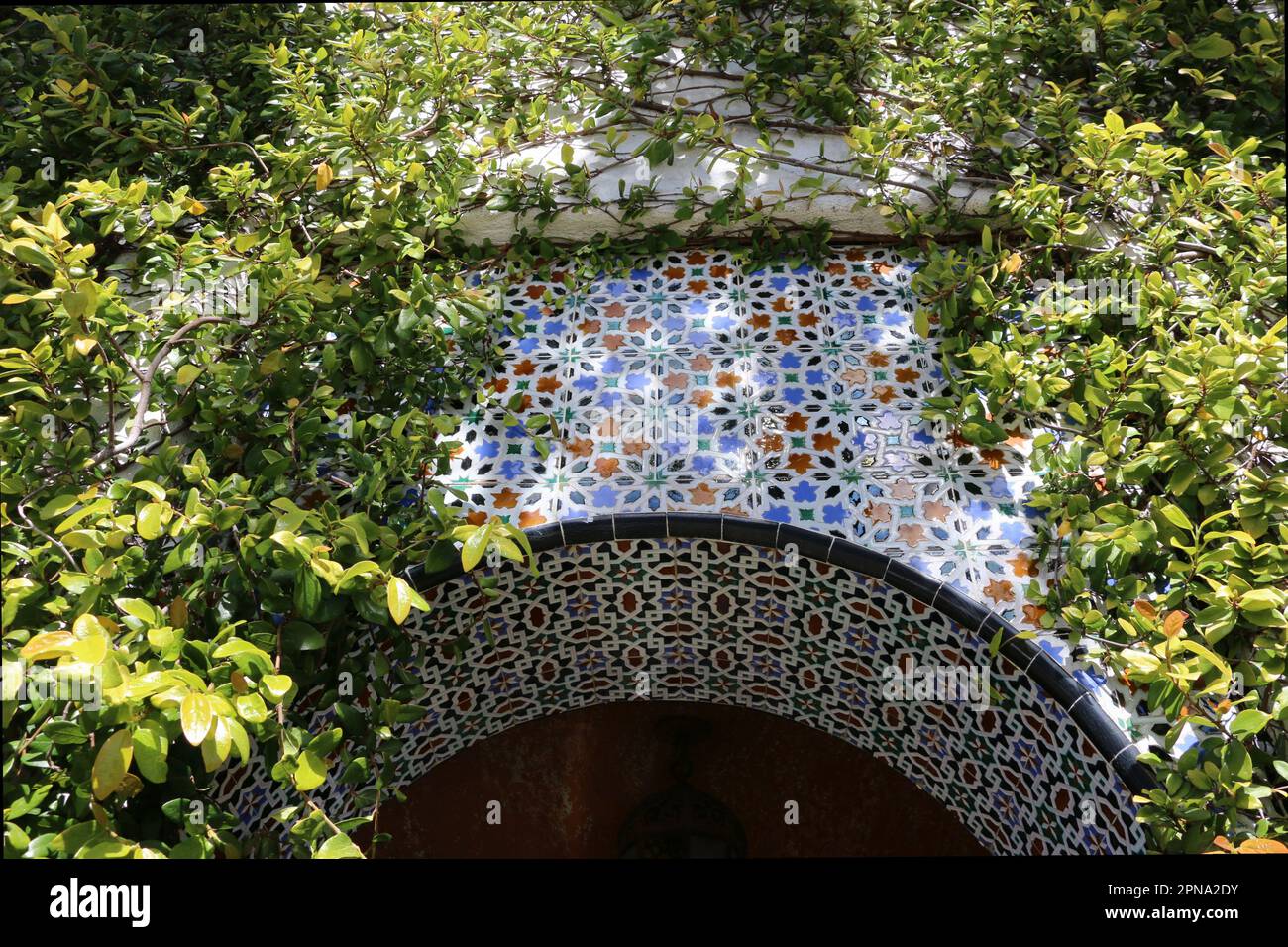 Bellissimo ingresso ad arco, decorato in un mosaico di piastrelle dipinte, incorniciato da alberi, nell'incantevole villaggio balneare di Carmel-by-the-Sea, CA. Foto Stock