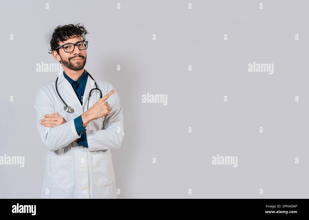 Medico sorridente che punta il dito isolato. Medico che indica uno spazio bianco isolato. Medico giovane che punta il dito in uno spazio vuoto Foto Stock