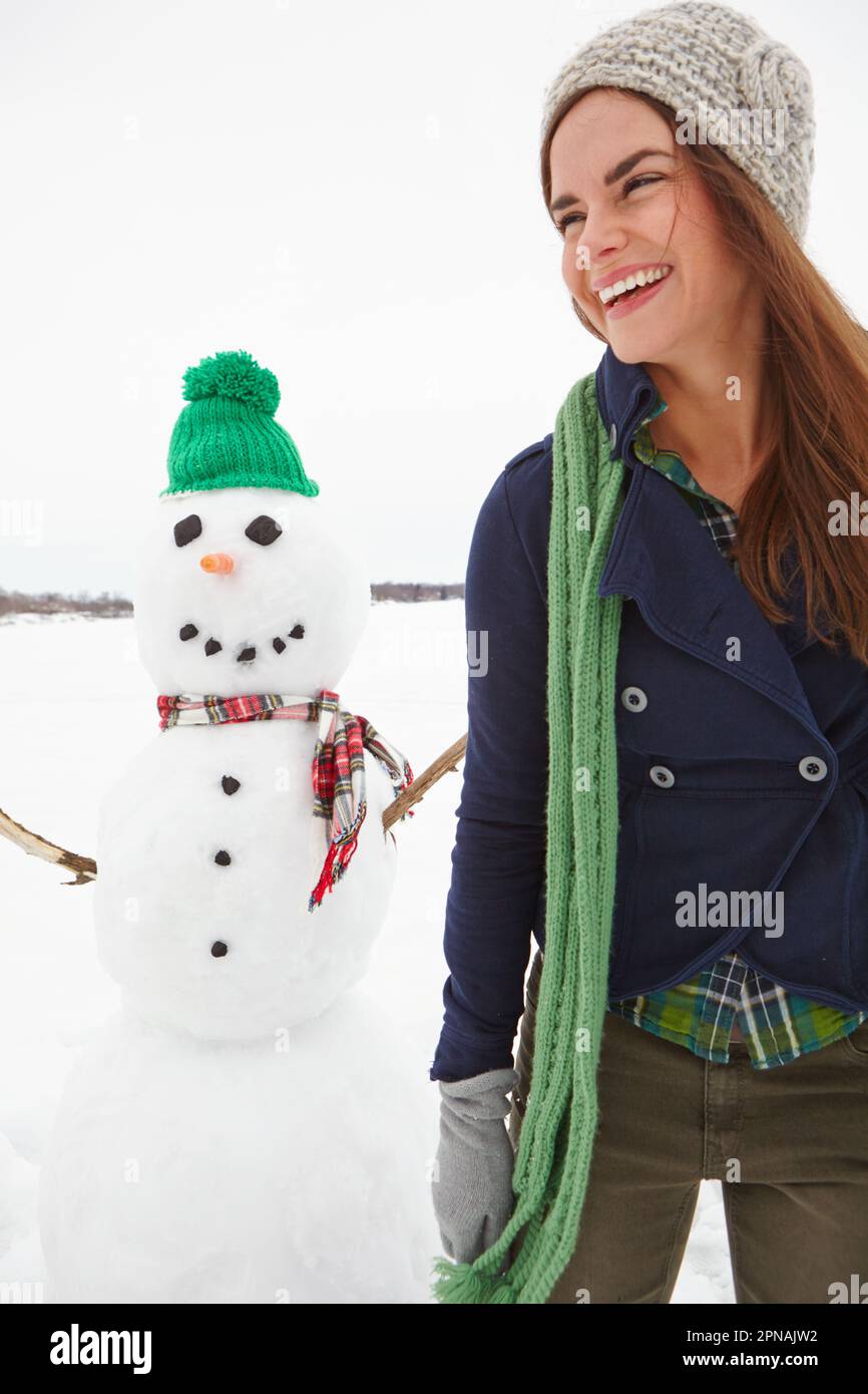 Fare nuovi amici. Un colpo di tre quarti di lunghezza di una giovane donna in piedi davanti a un pupazzo di neve. Foto Stock